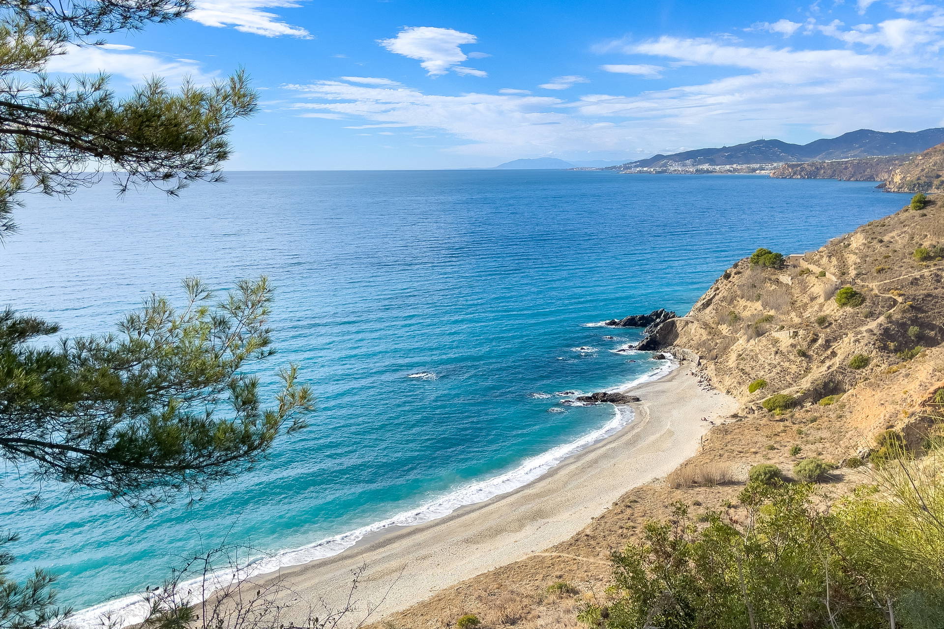 Widok z góry na turkusowe morze, piaszczystą plażę i skaliste wybrzeże Hiszpanii.