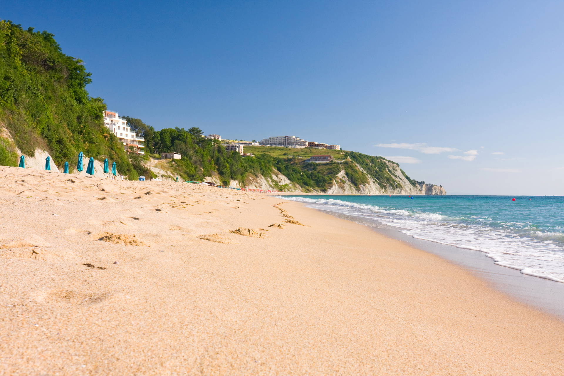 Piaszczysta plaża i budynki na klifie.