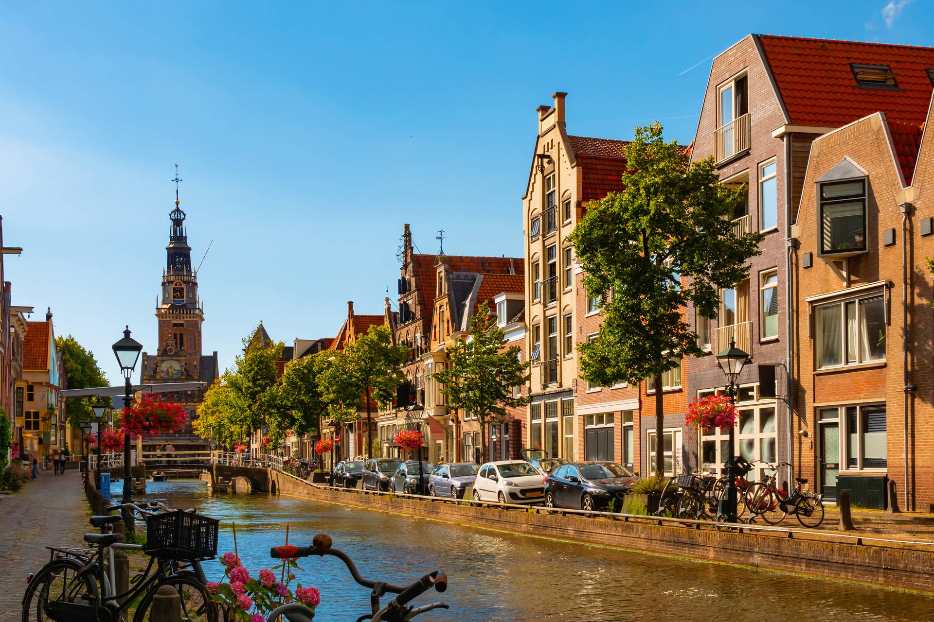 Kanał w Alkmaar z rowerami, samochodami i wieżą kościelną w tle.