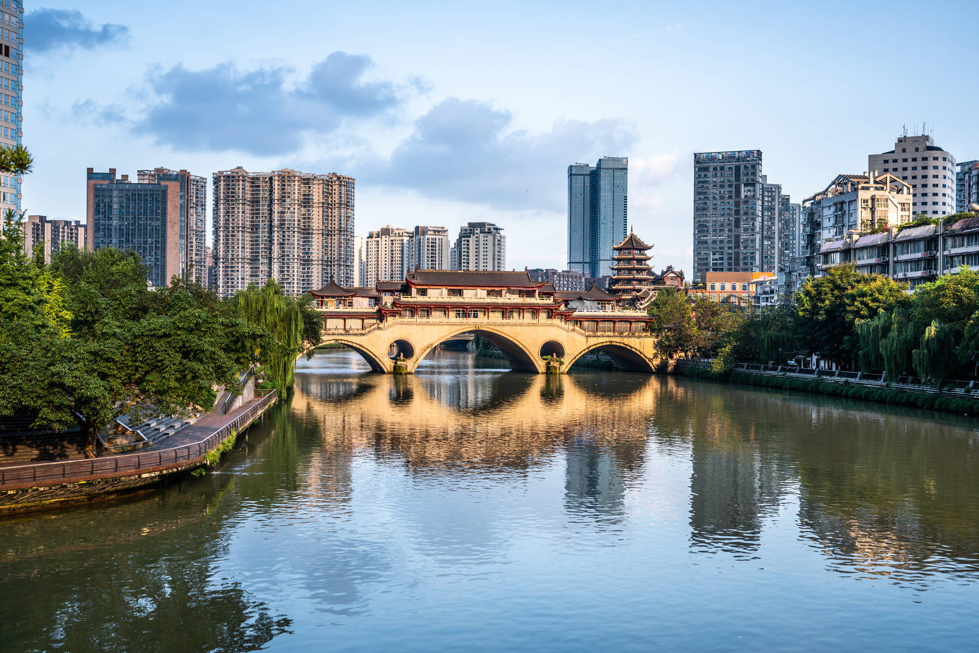 Most Anshun w Chengdu i jego odbicie w rzece. W tle zabudowa miejska.