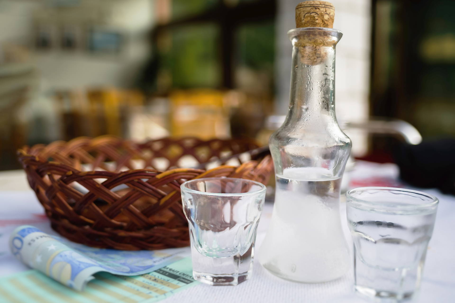 Butelka ouzo, dwa kieliszki i banknot leżą na stole.