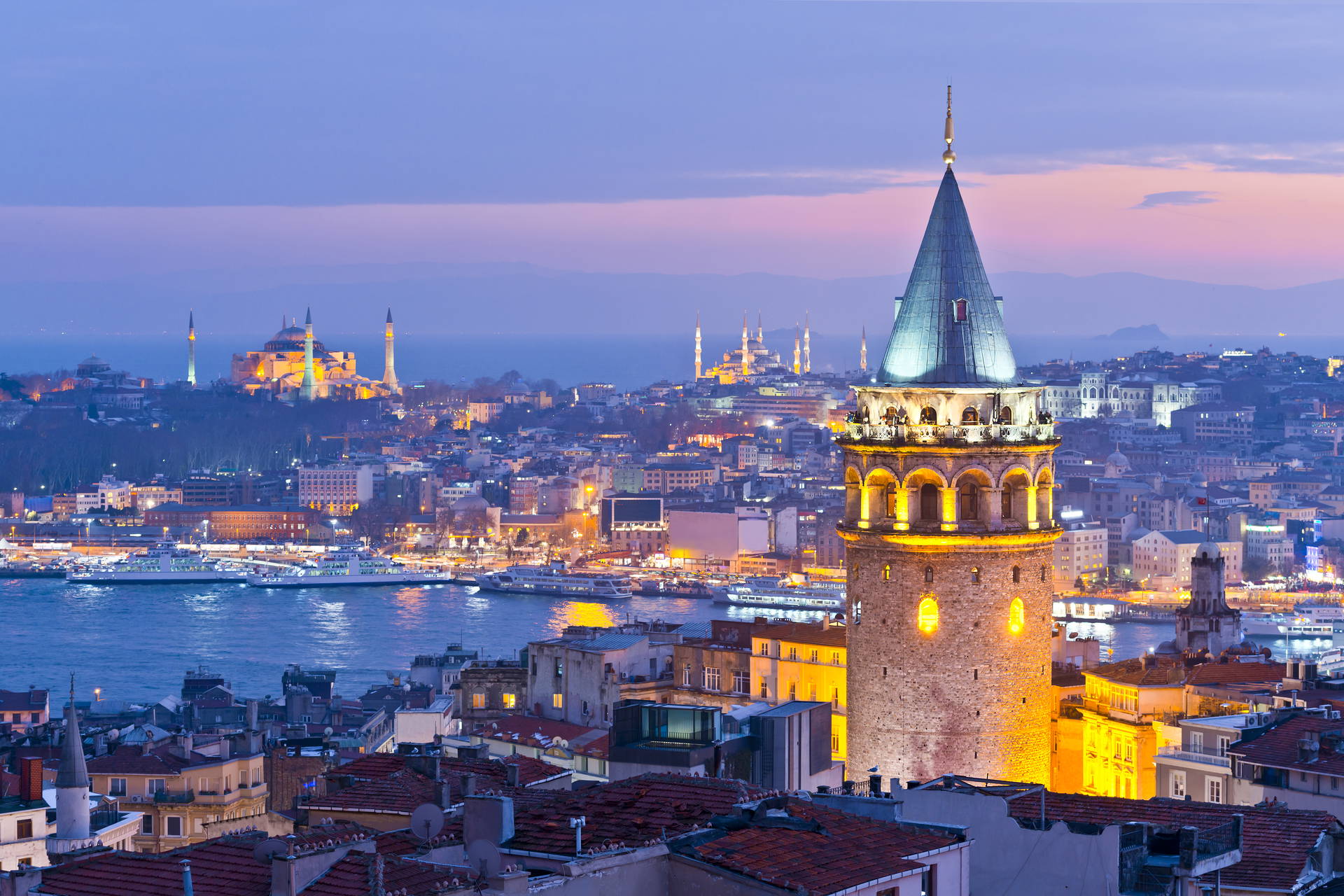 Wieczorna panorama Stambułu z oświetloną Wieżą Galata na pierwszym planie oraz Hagia Sophia i cieśniną Bosfor w tle.