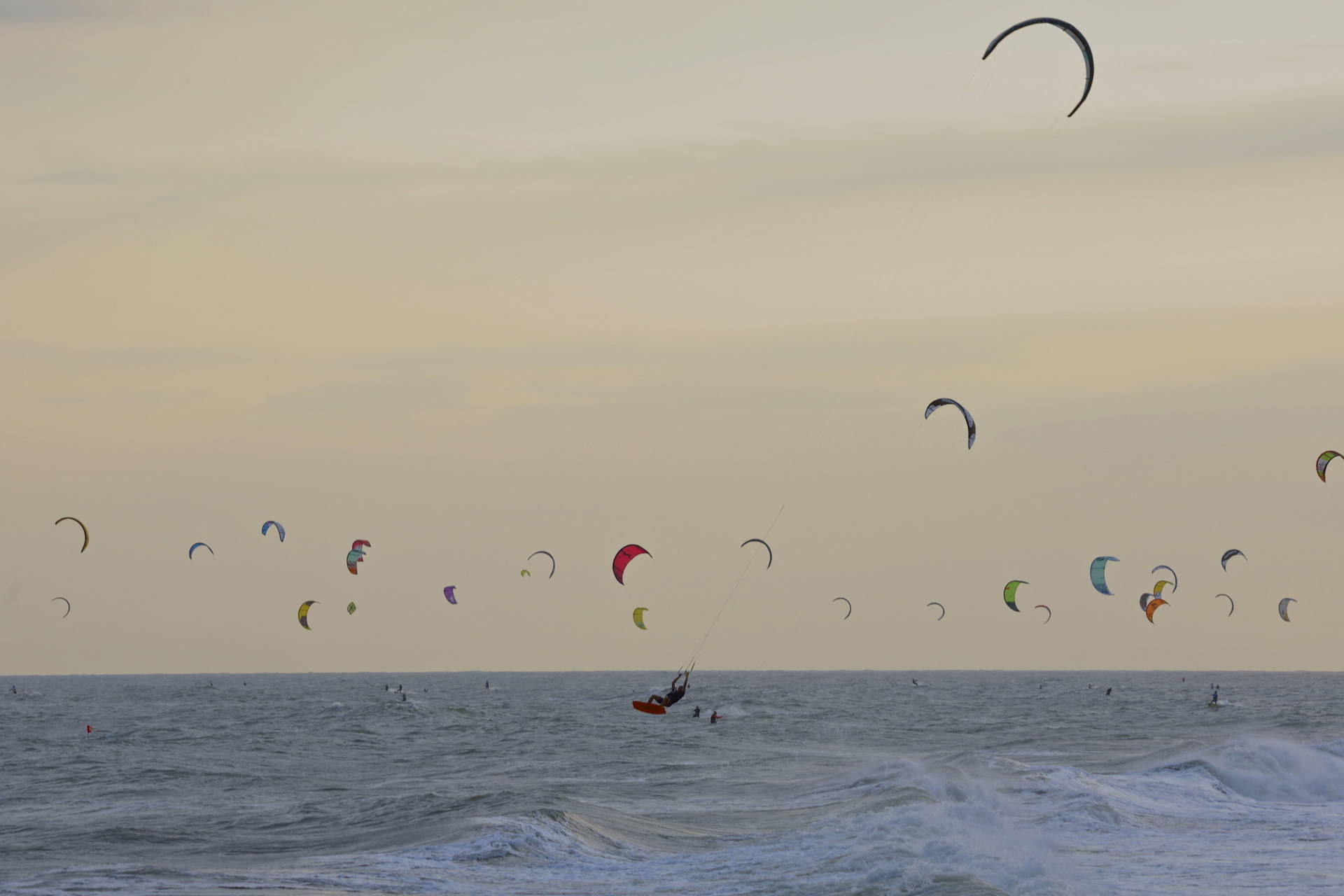 Kitesurferzy pływają po wzburzonym morzu. W tle pochmurne niebo.