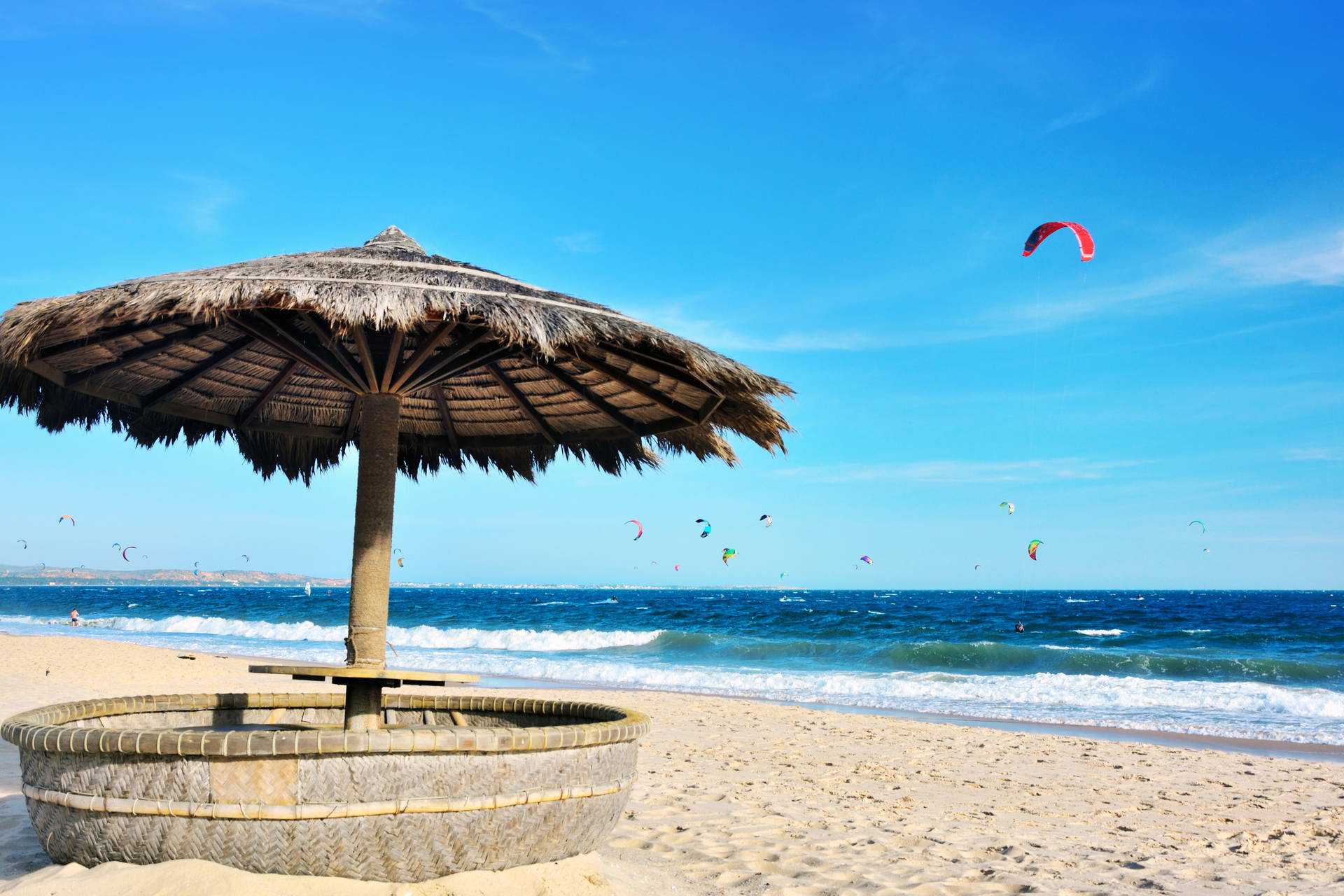 Parasol ze słomy na plaży i kitesurferzy na morzu.