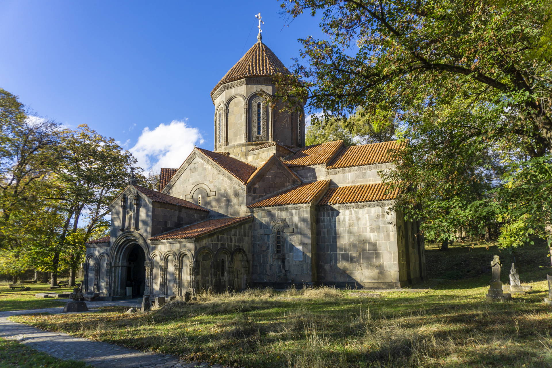 Kamienny klasztor Manglisi w Gruzji z pomarańczową dachówką i kopułą, otoczony zielenią w słoneczny dzień.