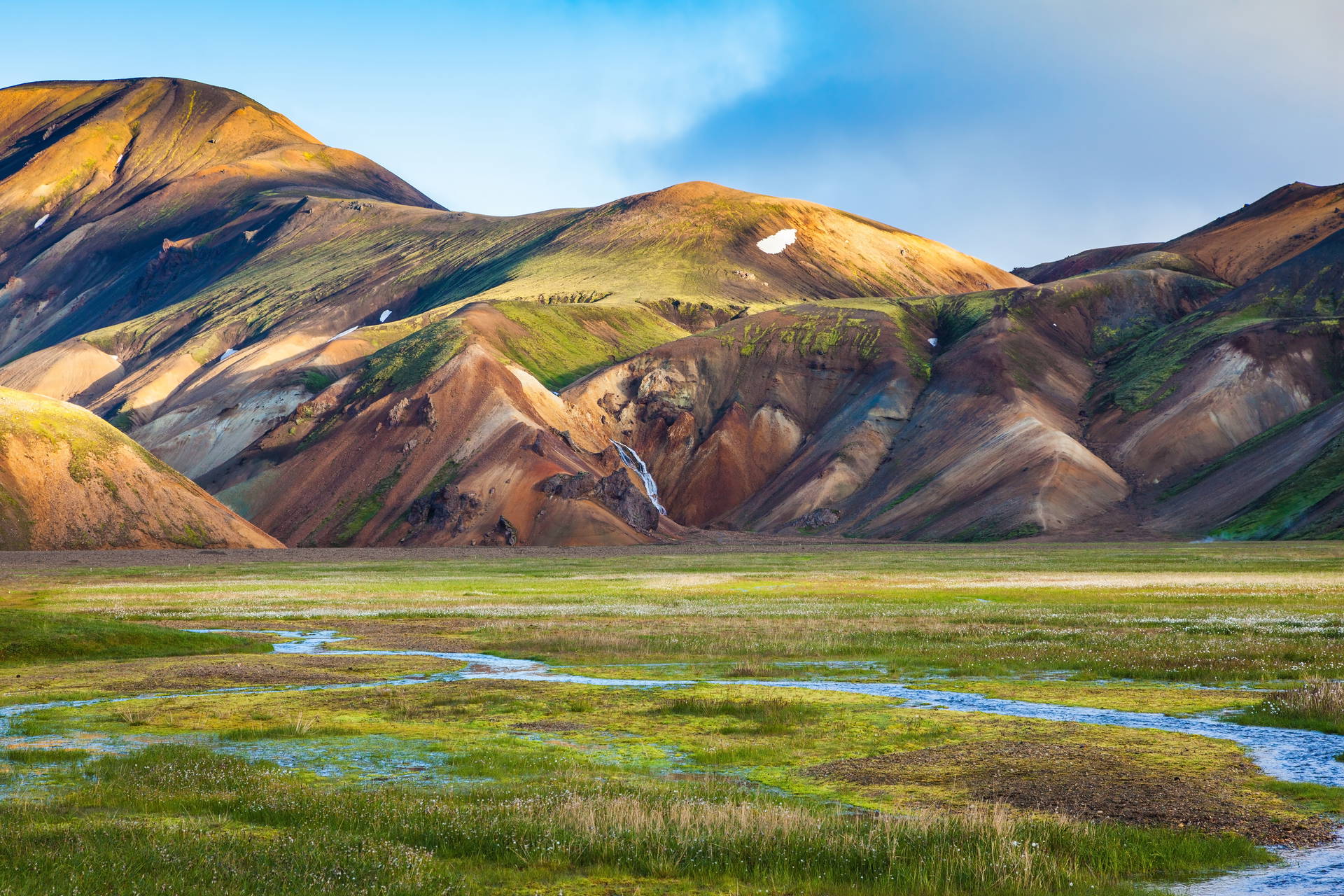 Zielona dolina z potokiem na tle kolorowych, tęczowych gór Landmannalaugar na Islandii.