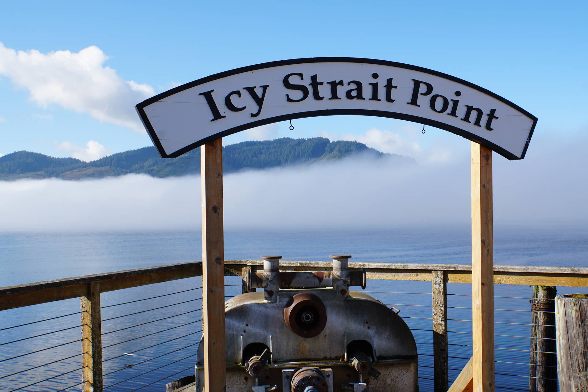 Znak "Icy Strait Point" na pomoście, w tle zamglona woda i zalesione wzgórza.