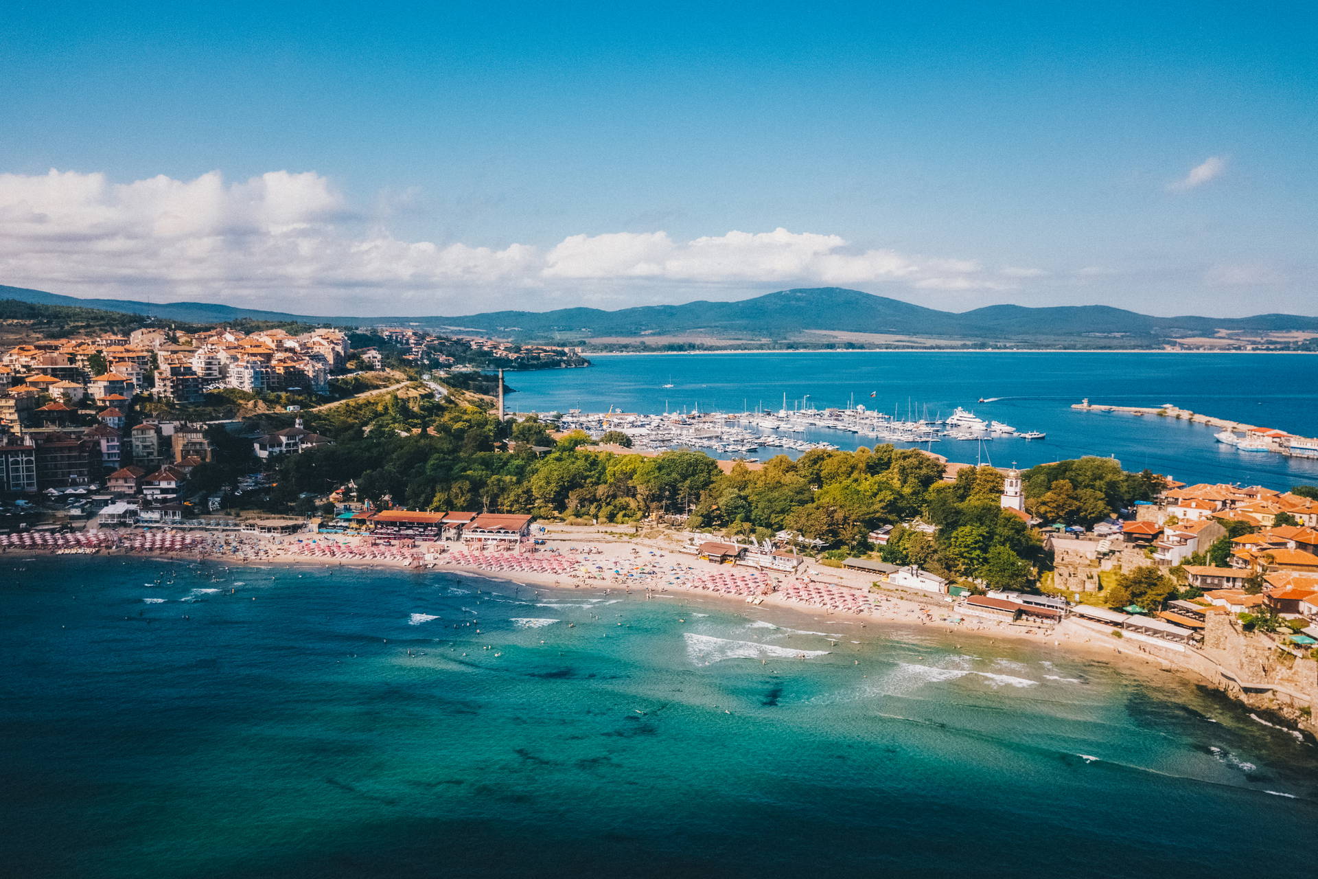 Widok z lotu ptaka na Sozopol w Bułgarii: piaszczysta plaża, turkusowe morze, miasto i marina pełna jachtów.