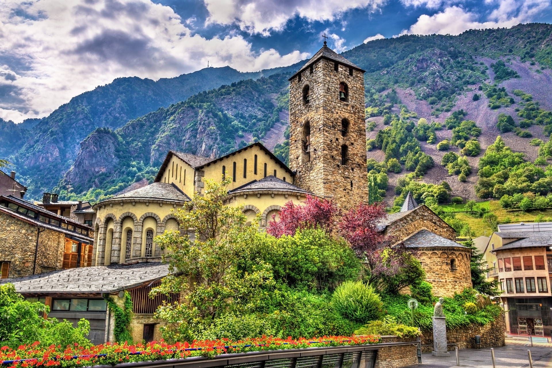 Kościół Sant Esteve w Andorra la Vella. Kamienna świątynia z wysoką wieżą na tle zielonych gór.