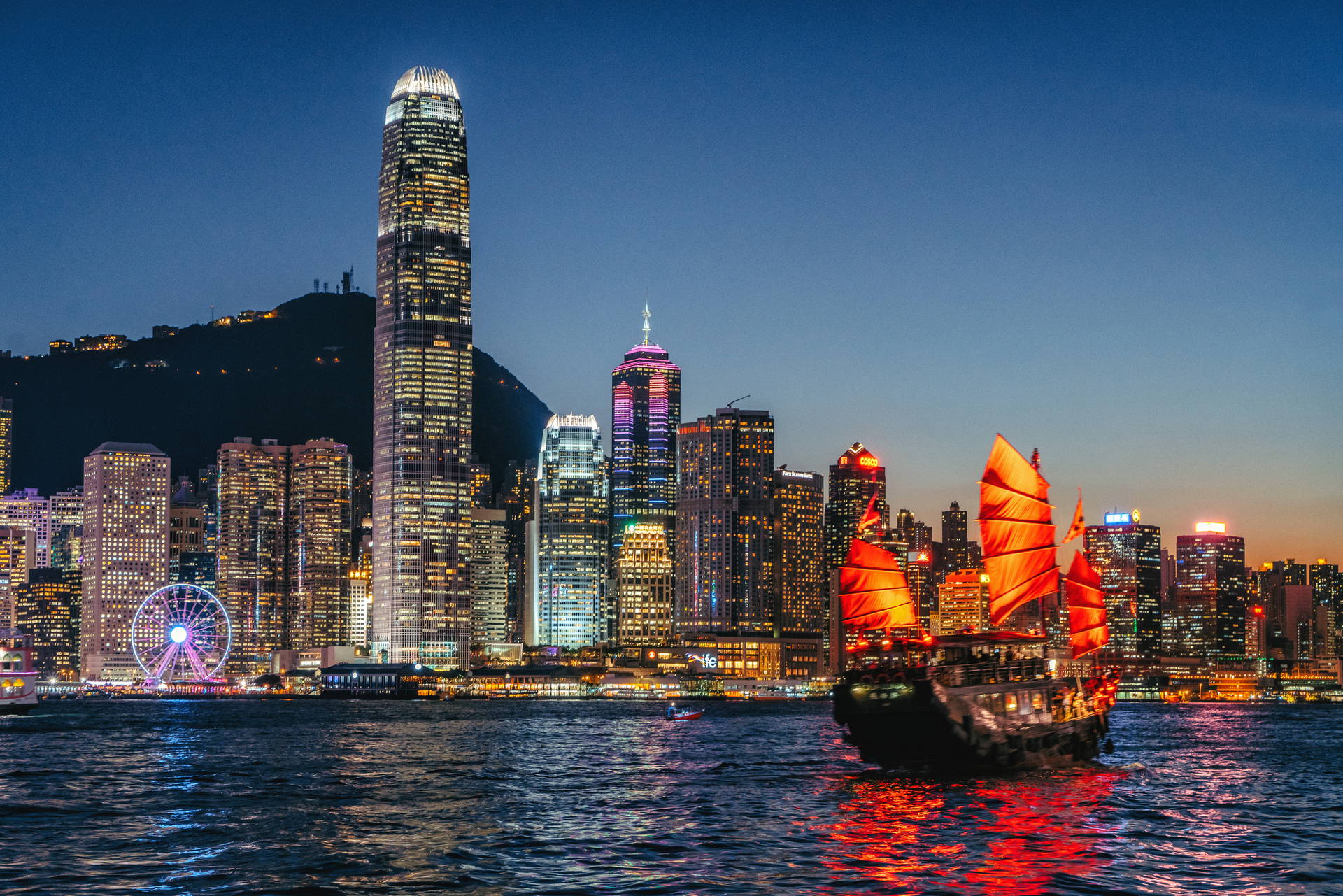Nocna panorama Hongkongu z tradycyjnymi łodziami na wodzie.