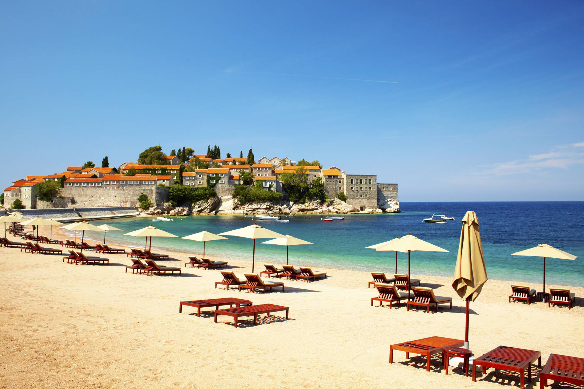 Plaża ze Sveti Stefan w tle: leżaki, parasole i zabudowana wyspa.