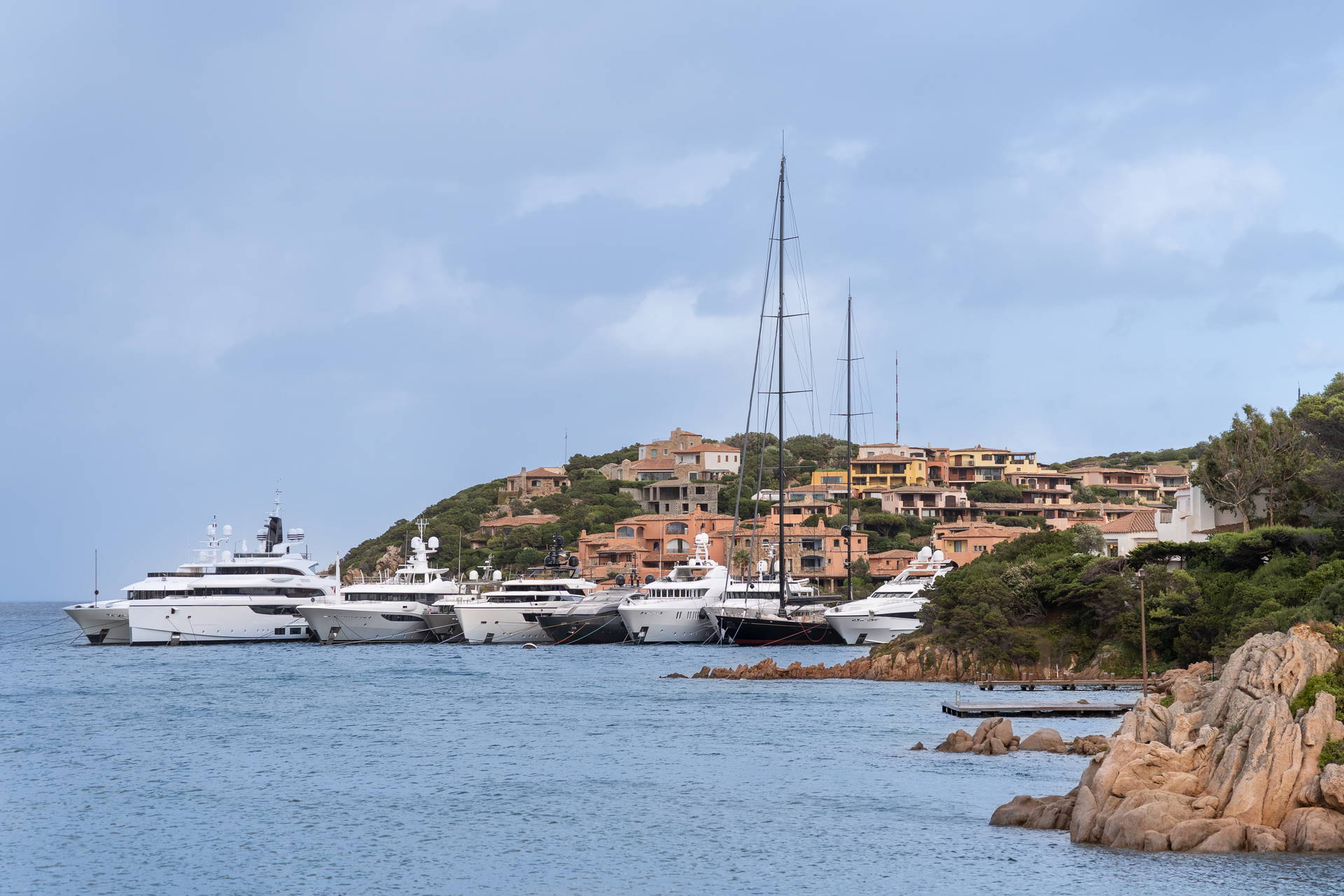 Zatoka z luksusowymi jachtami i zabudowaniami na wzgórzu.