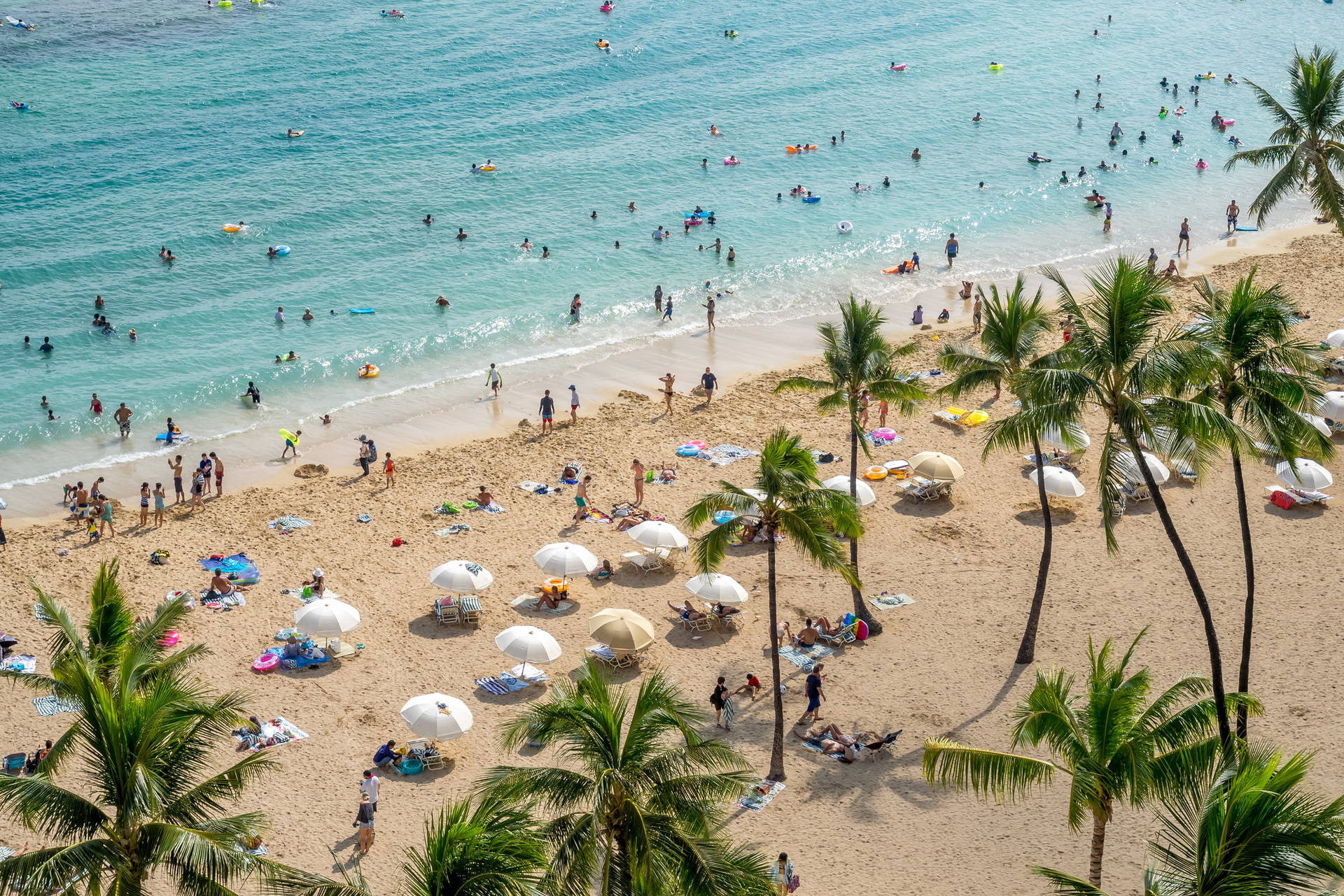 Plaża Waikiki na Hawajach z lotu ptaka. Widać opalających się ludzi, palmy i ocean.
