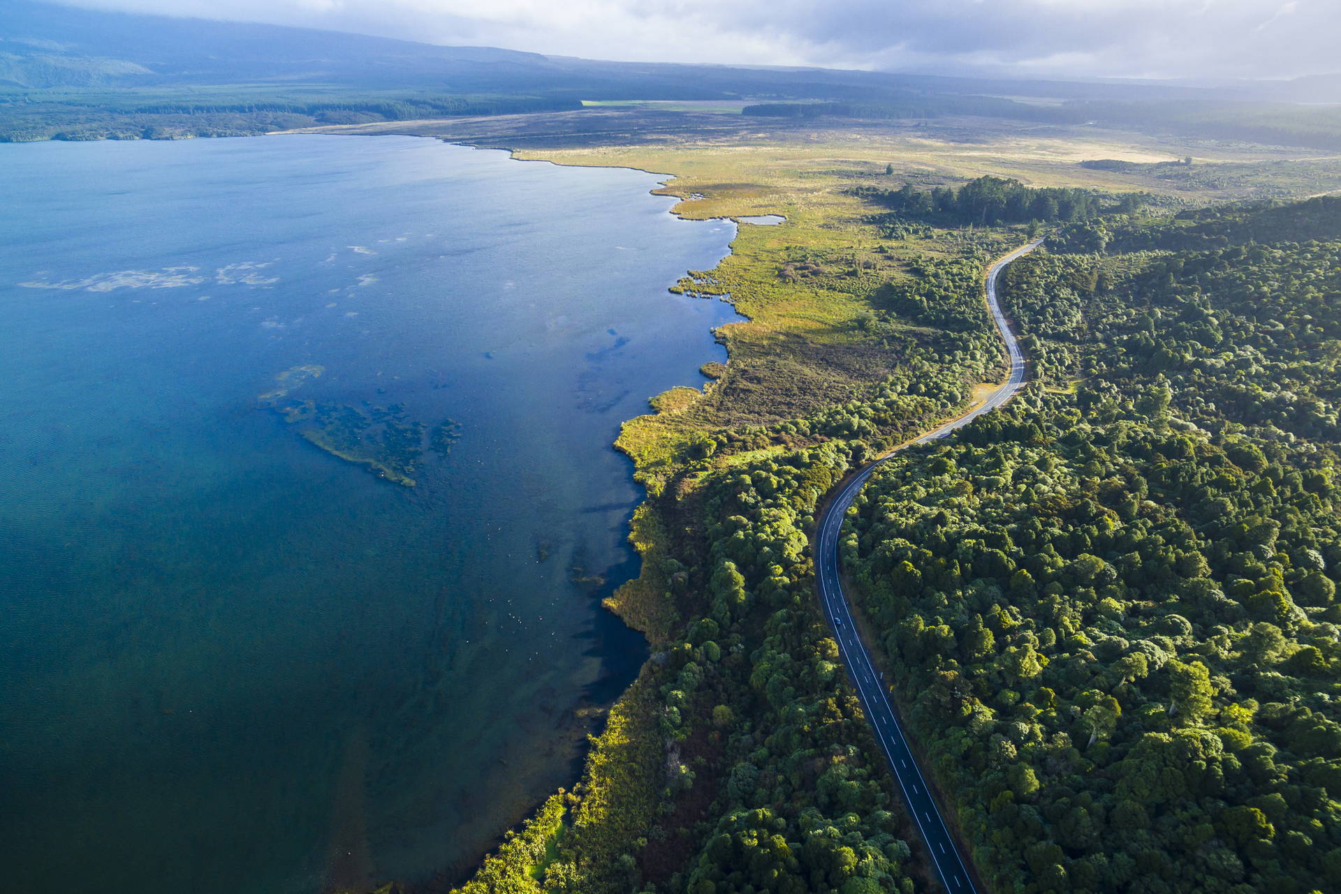 Jezioro otoczone lasem i wijącą się drogą, widok z lotu ptaka.