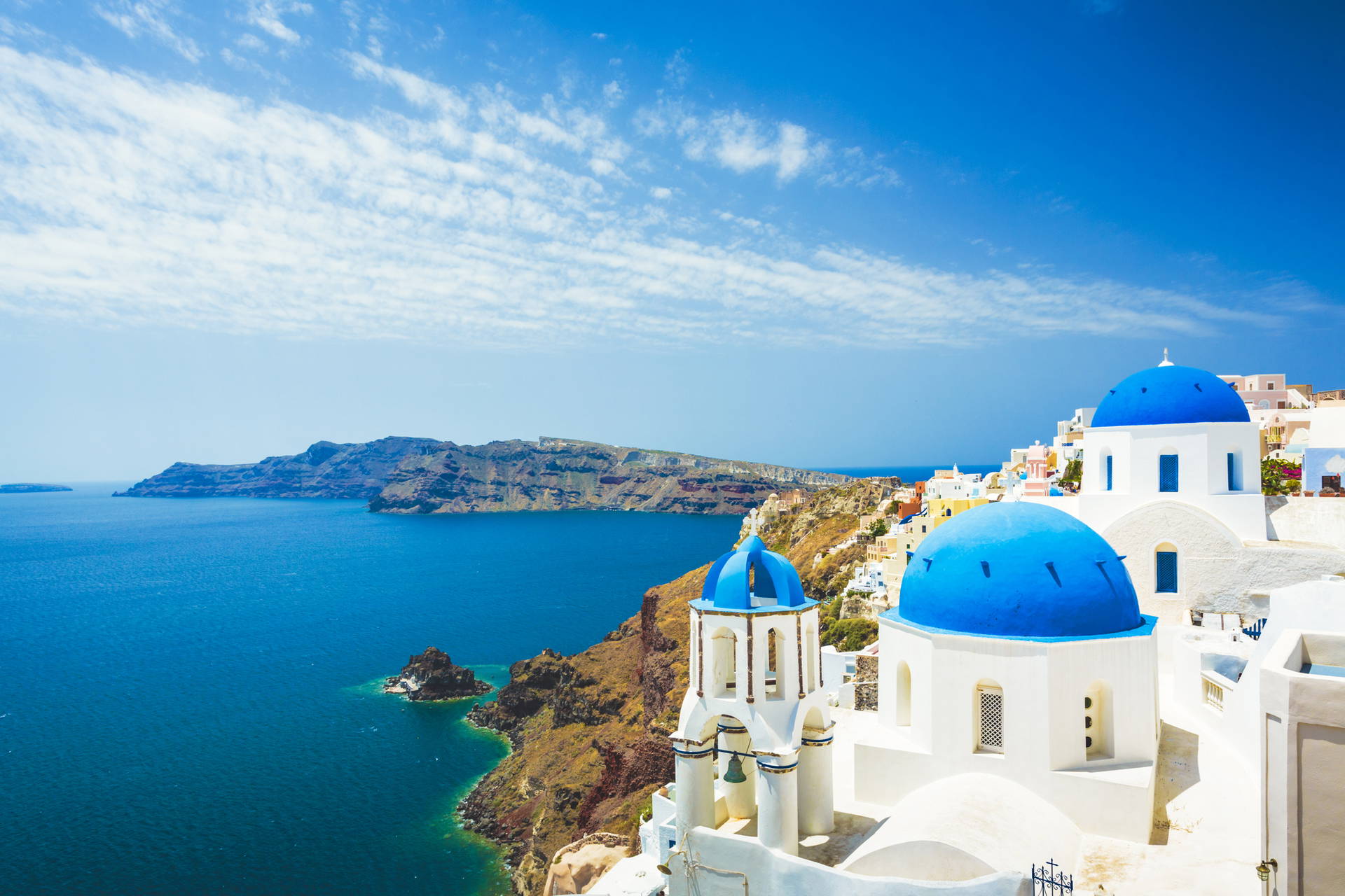 Santorini, Grecja. Białe budynki z niebieskimi kopułami nad morzem.