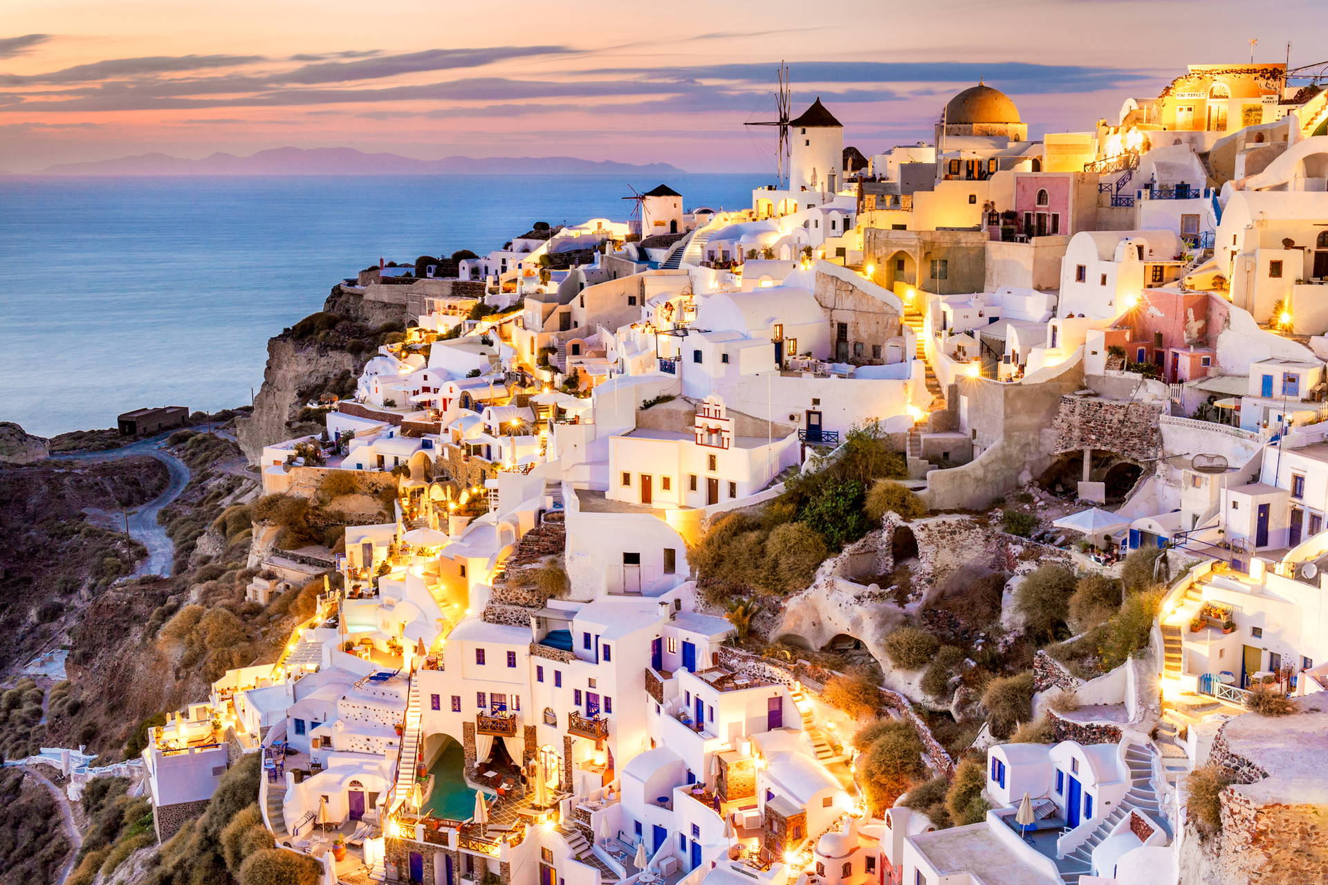 Santorini o zmierzchu: białe domy na klifie z widokiem na morze i wiatraki.