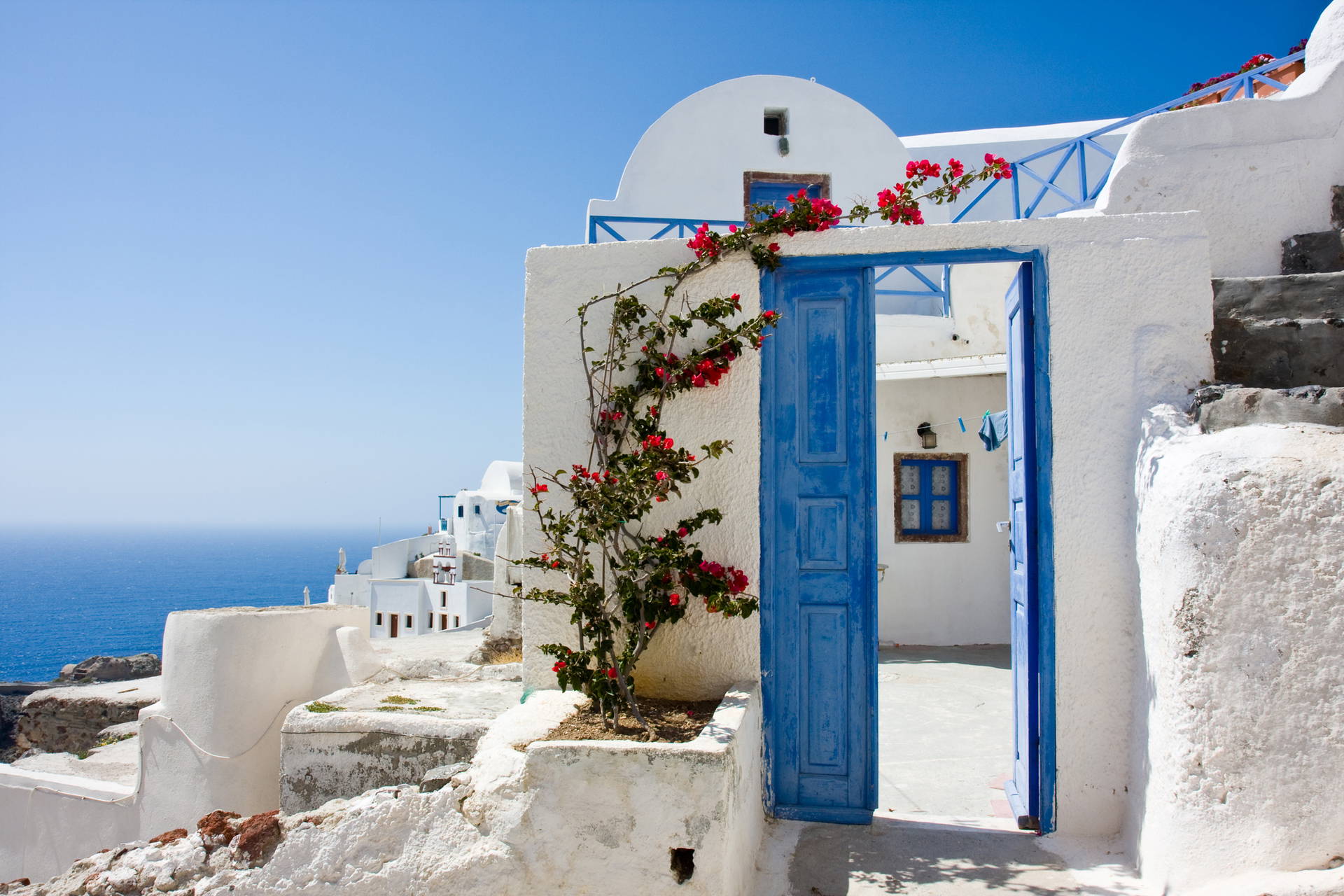 Biały budynek z niebieskimi drzwiami i kwiatami na Santorini.