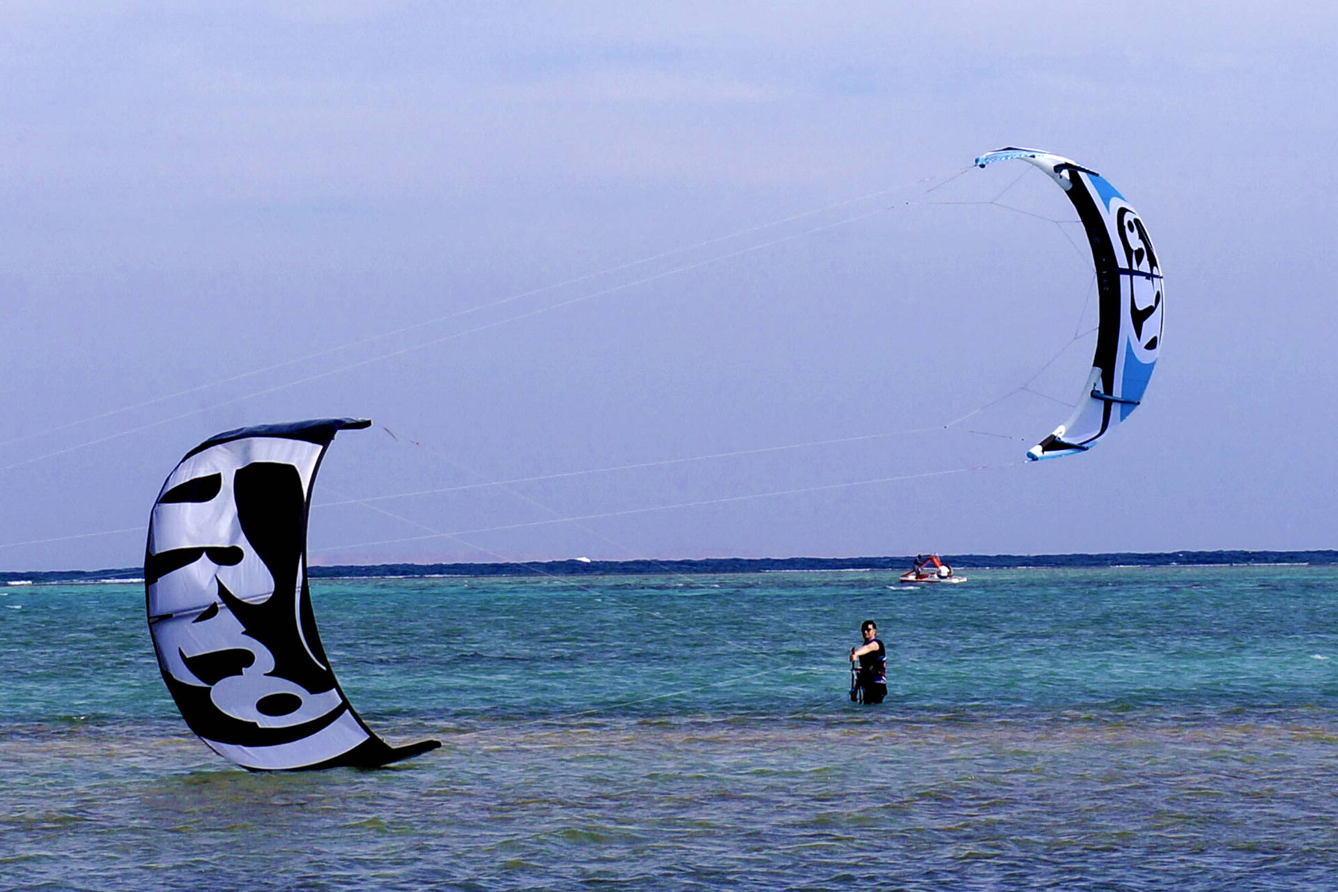 Dwie osoby uprawiają kitesurfing na morzu.