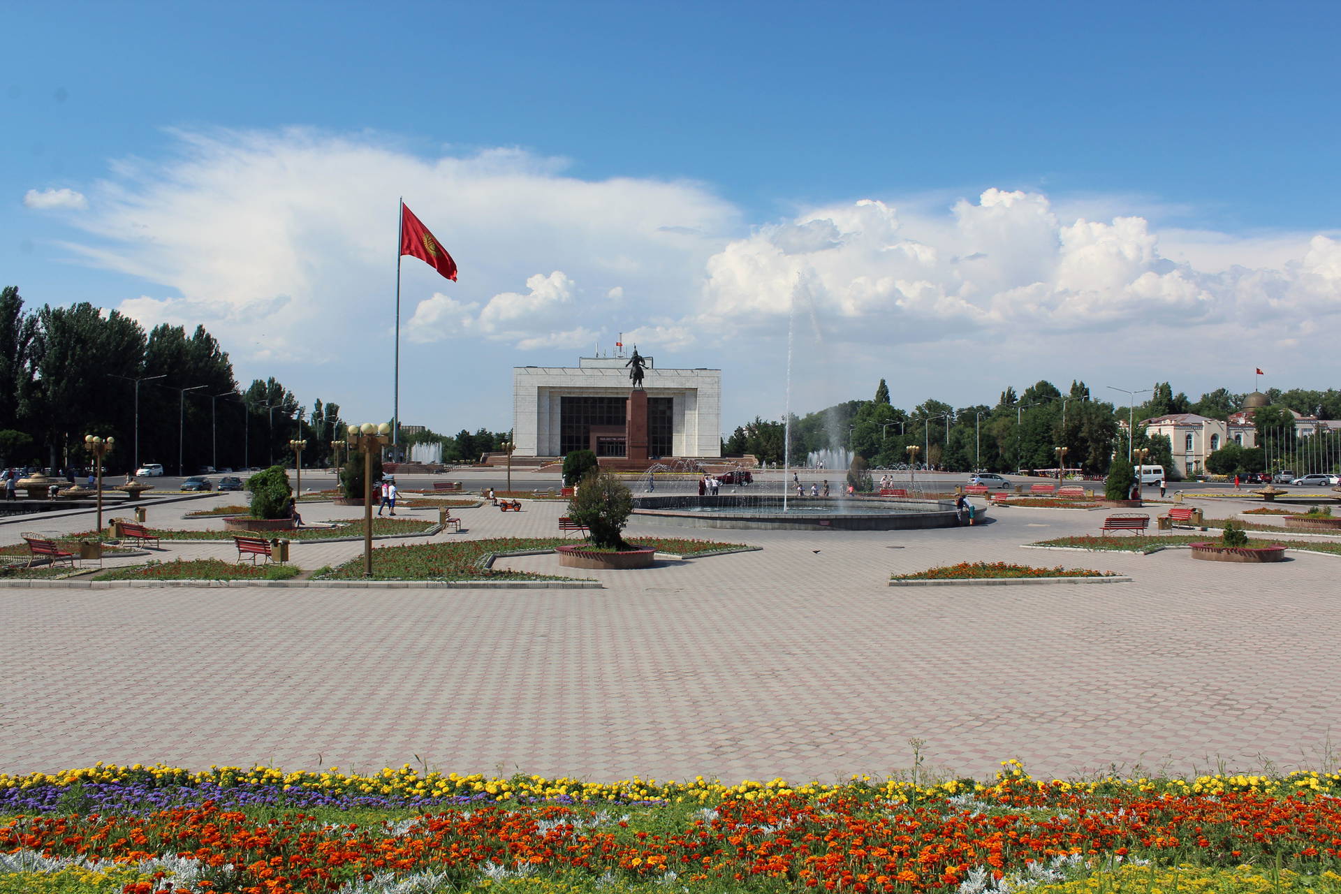 Plac Ala-Too w Biszkeku z flagą Kirgistanu i fontanną. W tle budynek.
