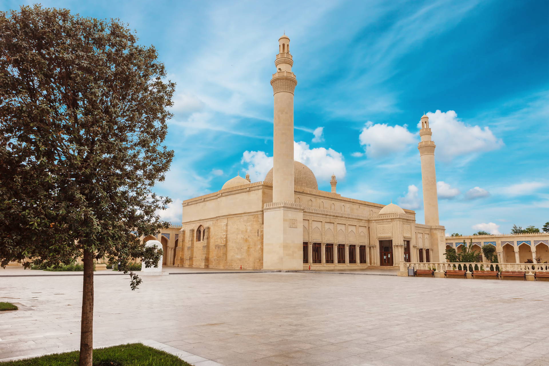 Meczet Bibi-Heybat w Baku z dwoma minaretami na dużym dziedzińcu, na tle błękitnego nieba z chmurami.
