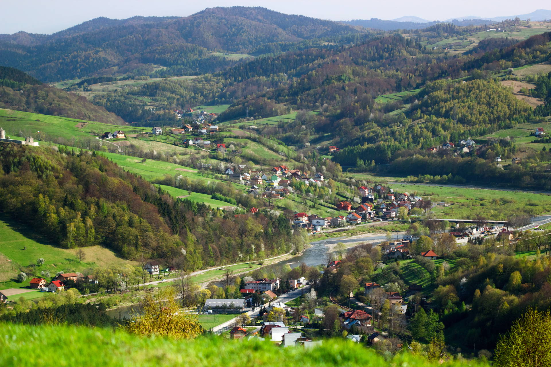 Krajobraz górski z doliną, rzeką i zabudowaniami w tle.