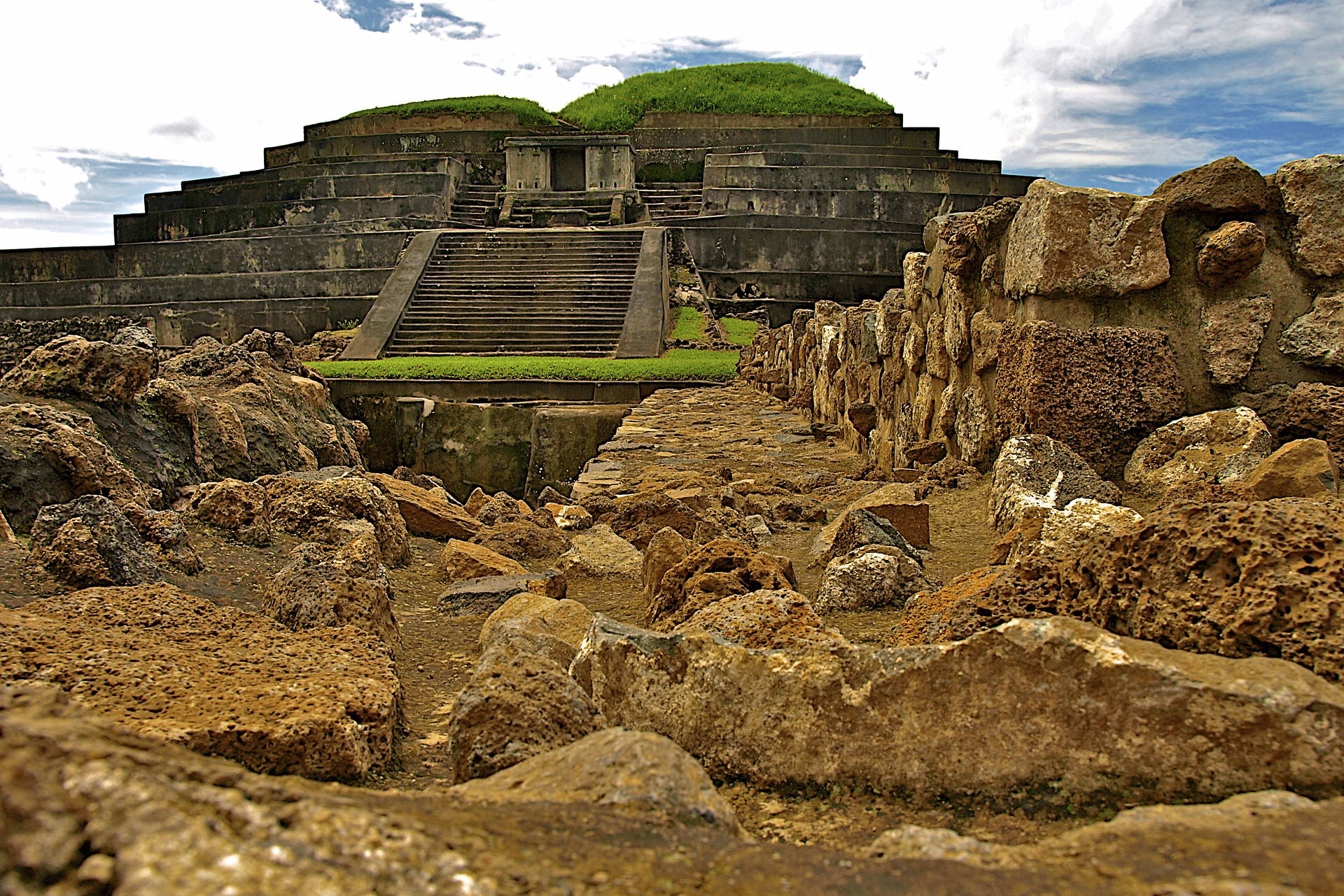 Ruiny starożytnej piramidy z kamiennymi schodami i porośniętym wierzchołkiem.