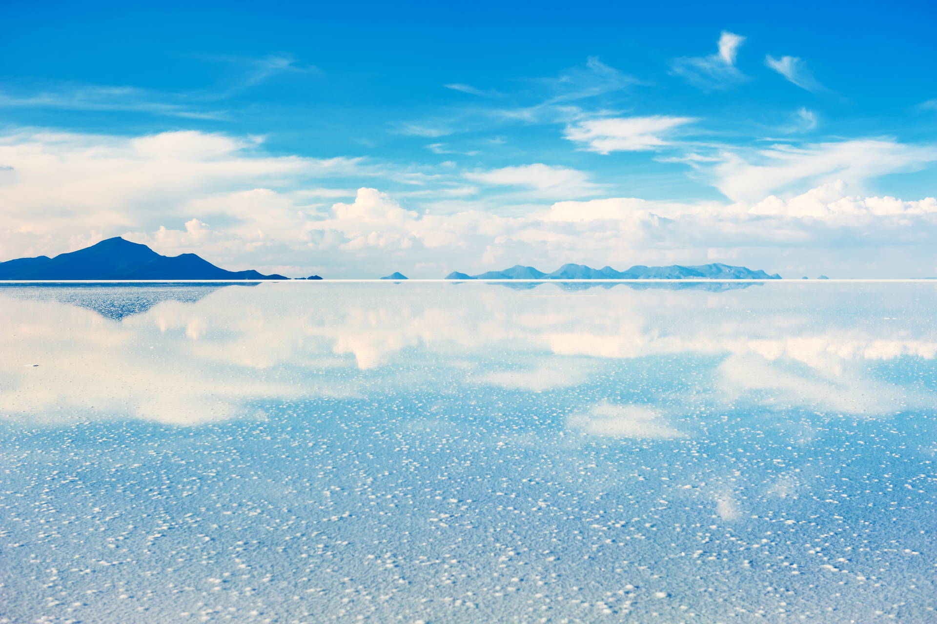 Pejzaż Salar de Uyuni z odbijającym się niebem i górami.