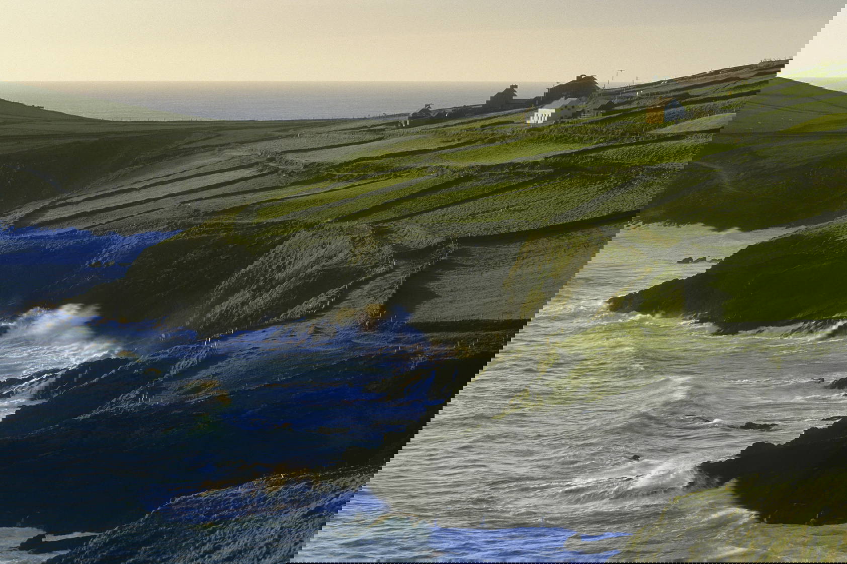 Klifowe wybrzeże z budynkami na wzgórzach, o które rozbijają się fale.