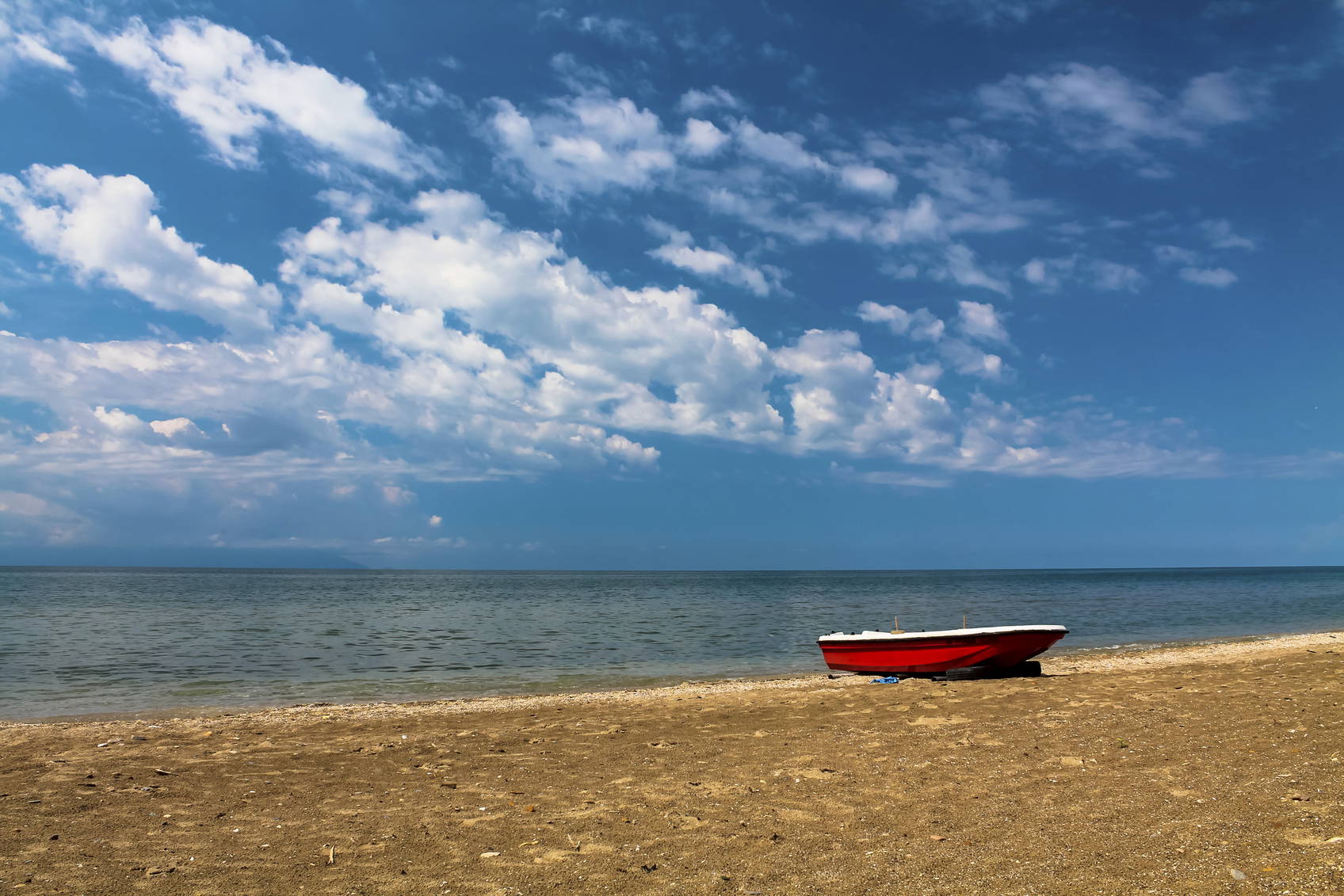 Czerwona łódź na piaszczystej plaży pod błękitnym niebem.