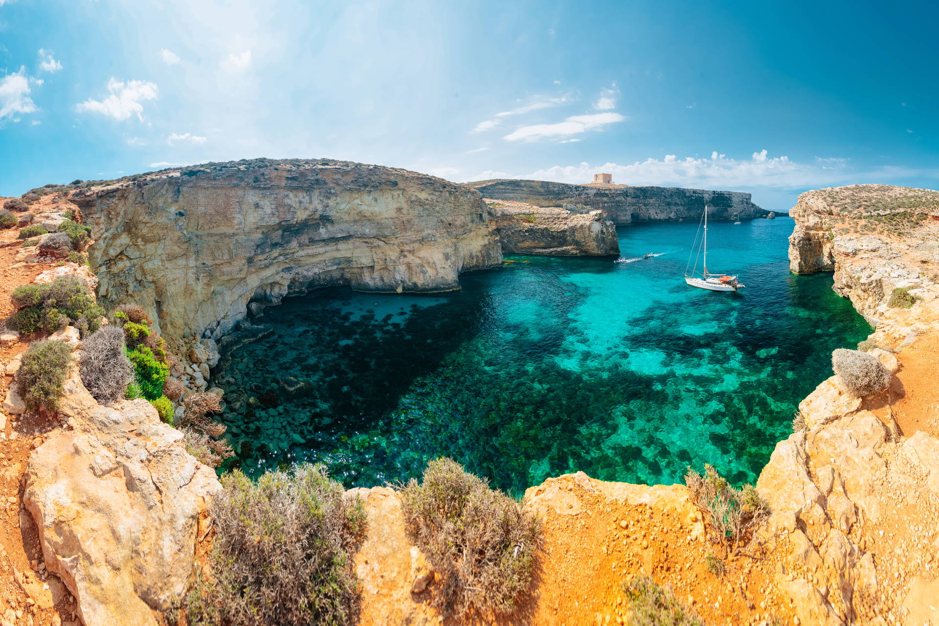 Panorama zatoki Comino na Malcie: klify i jacht na wodzie.