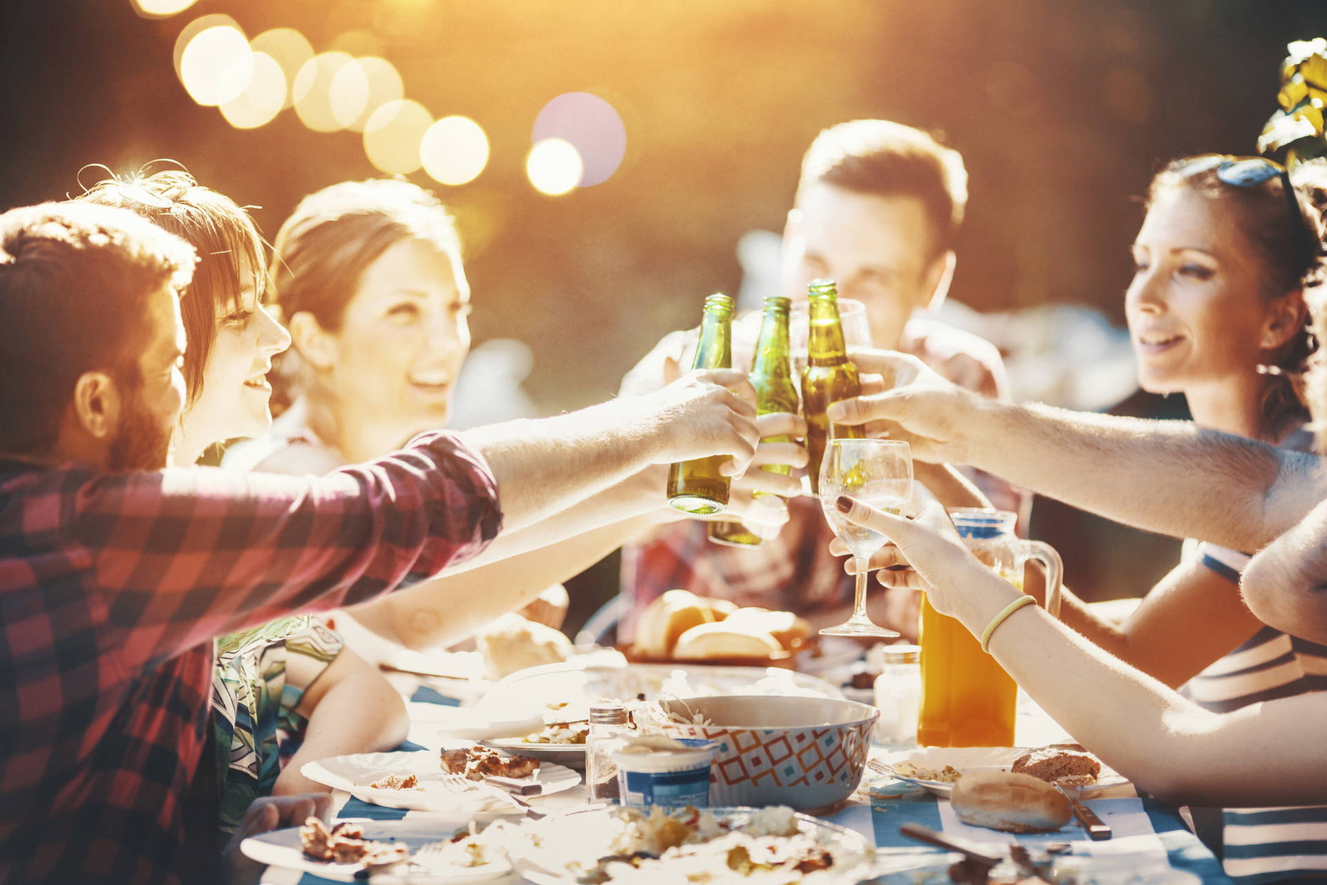 Grupa przyjaciół wznosi toast piwem i winem na przyjęciu w plenerze.