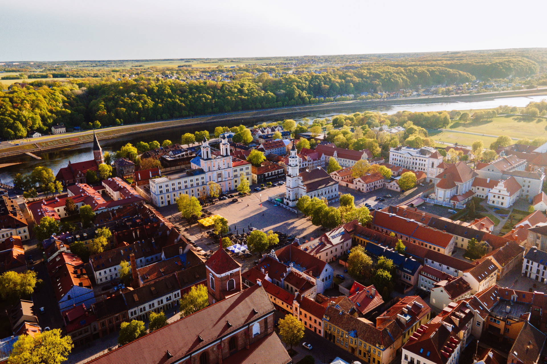 Panorama Kowna z czerwonymi dachami, zielenią drzew i rzeką Niemen w tle.