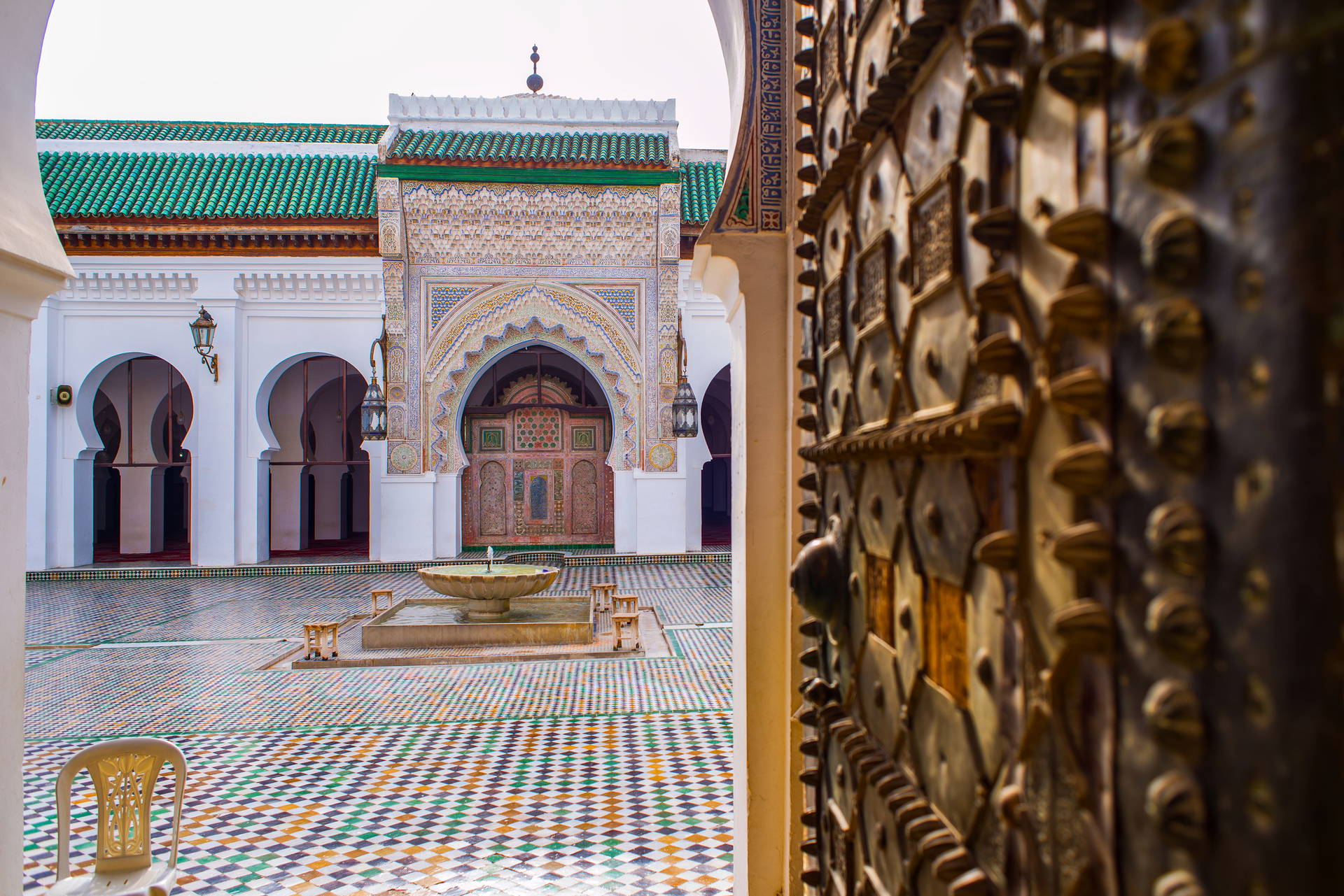 Dziedziniec Meczetu Andaluzjan w Fezie z fontanną i zdobionymi drzwiami.