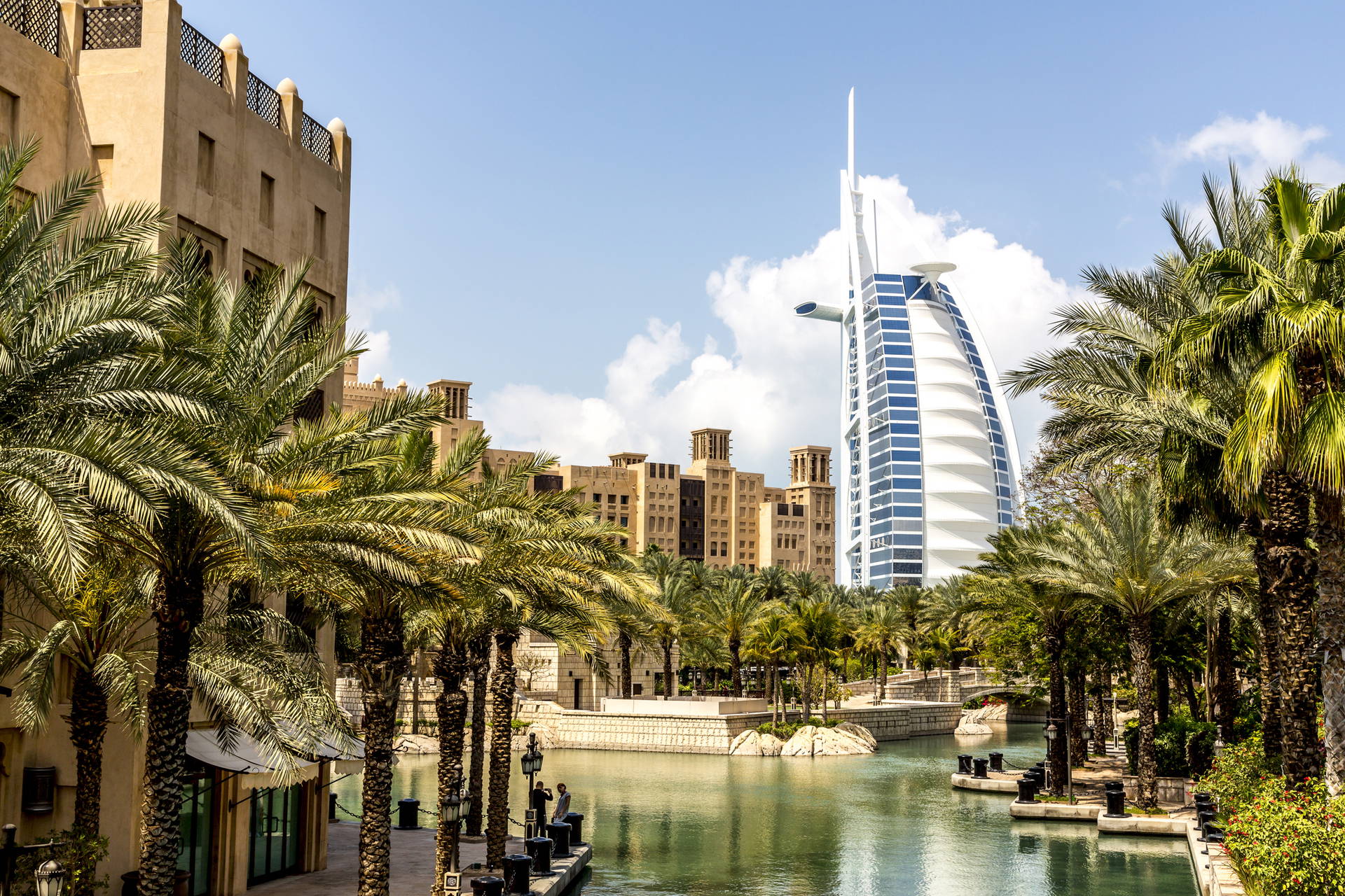Burj Al Arab w Dubaju widziany z kanału, otoczony palmami.