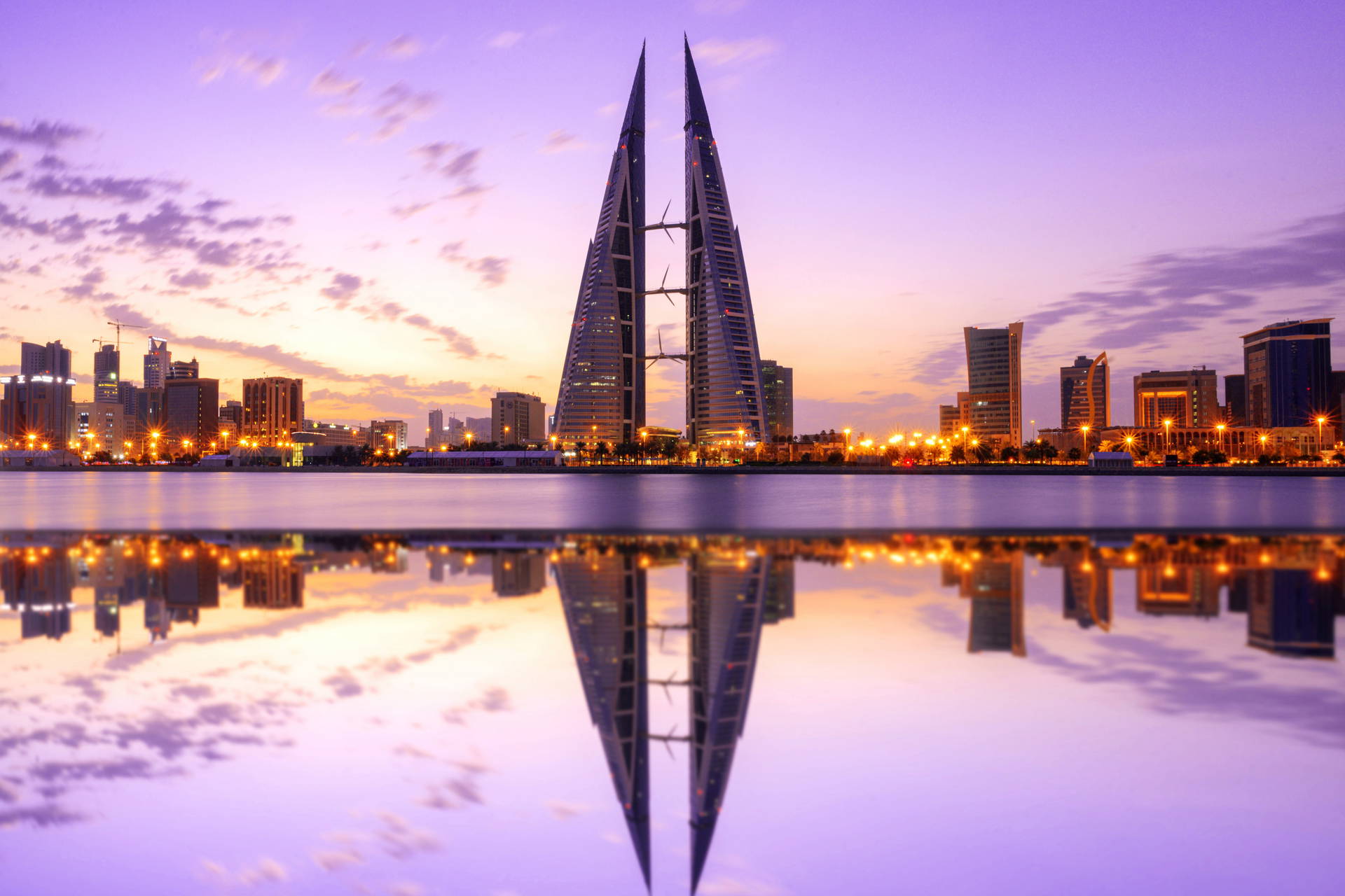Wieżowce Bahrain World Trade Center i ich odbicie w wodzie o zachodzie słońca.