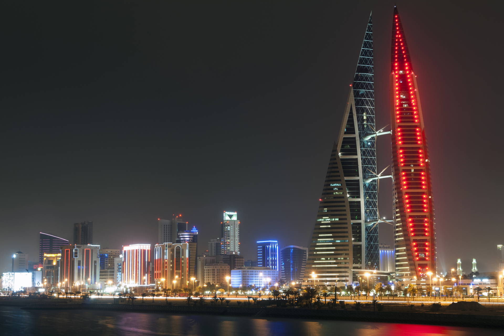 Wieżowce Bahrain World Trade Center oświetlone na tle nocnej panoramy Manamy. Jedna z wież jest czerwona.