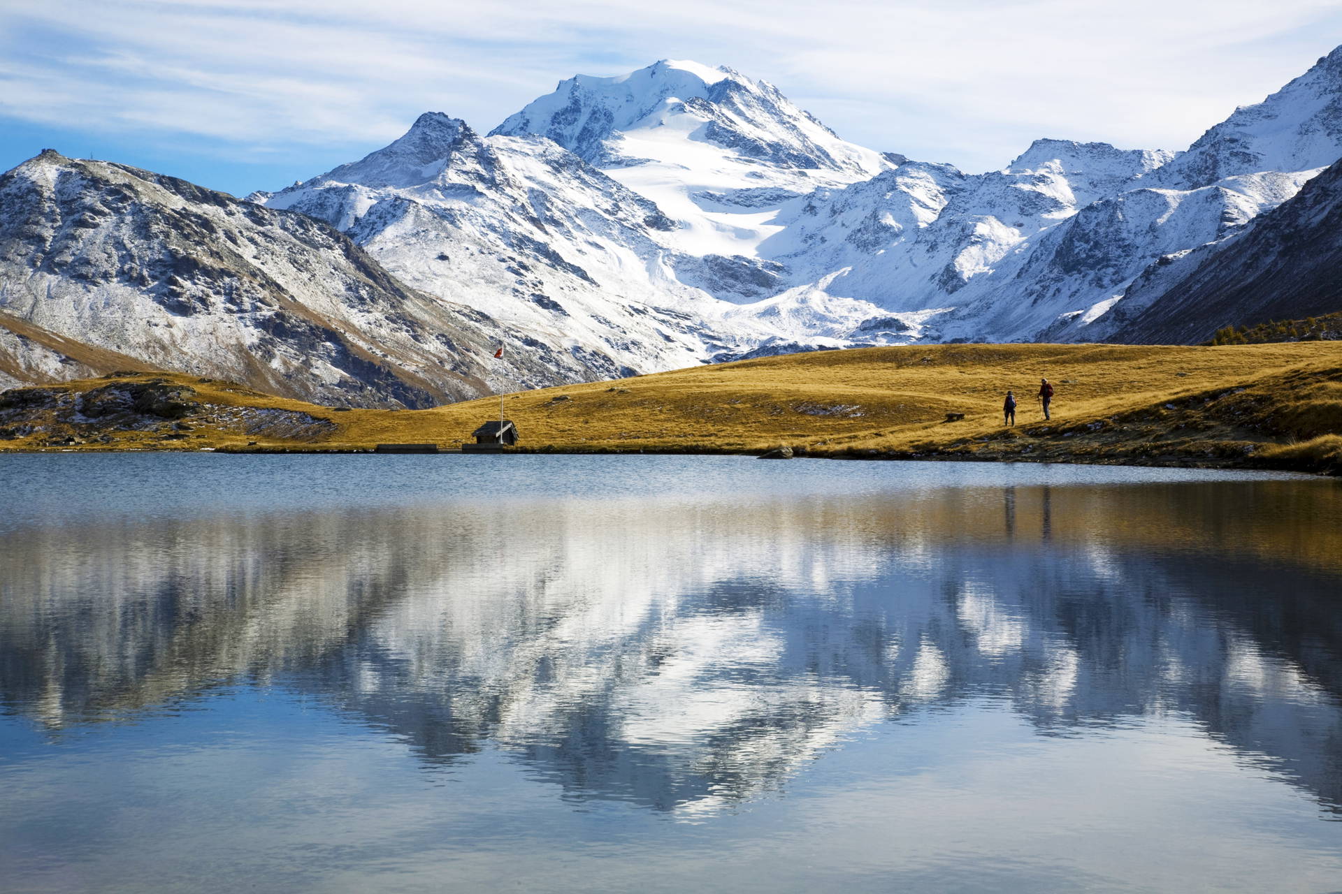Górski krajobraz z jeziorem, w którym odbijają się ośnieżone szczyty.