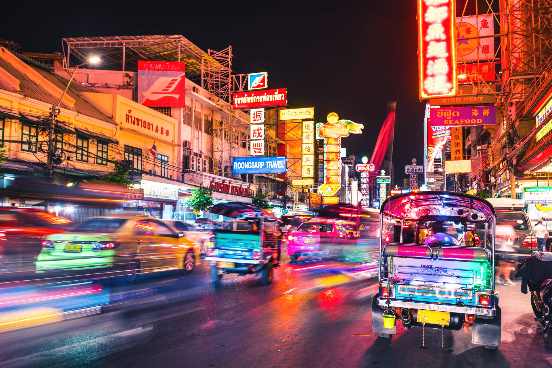 Nocna ulica w Chinatown w Bangkoku oświetlona neonami, z tuk-tukami.
