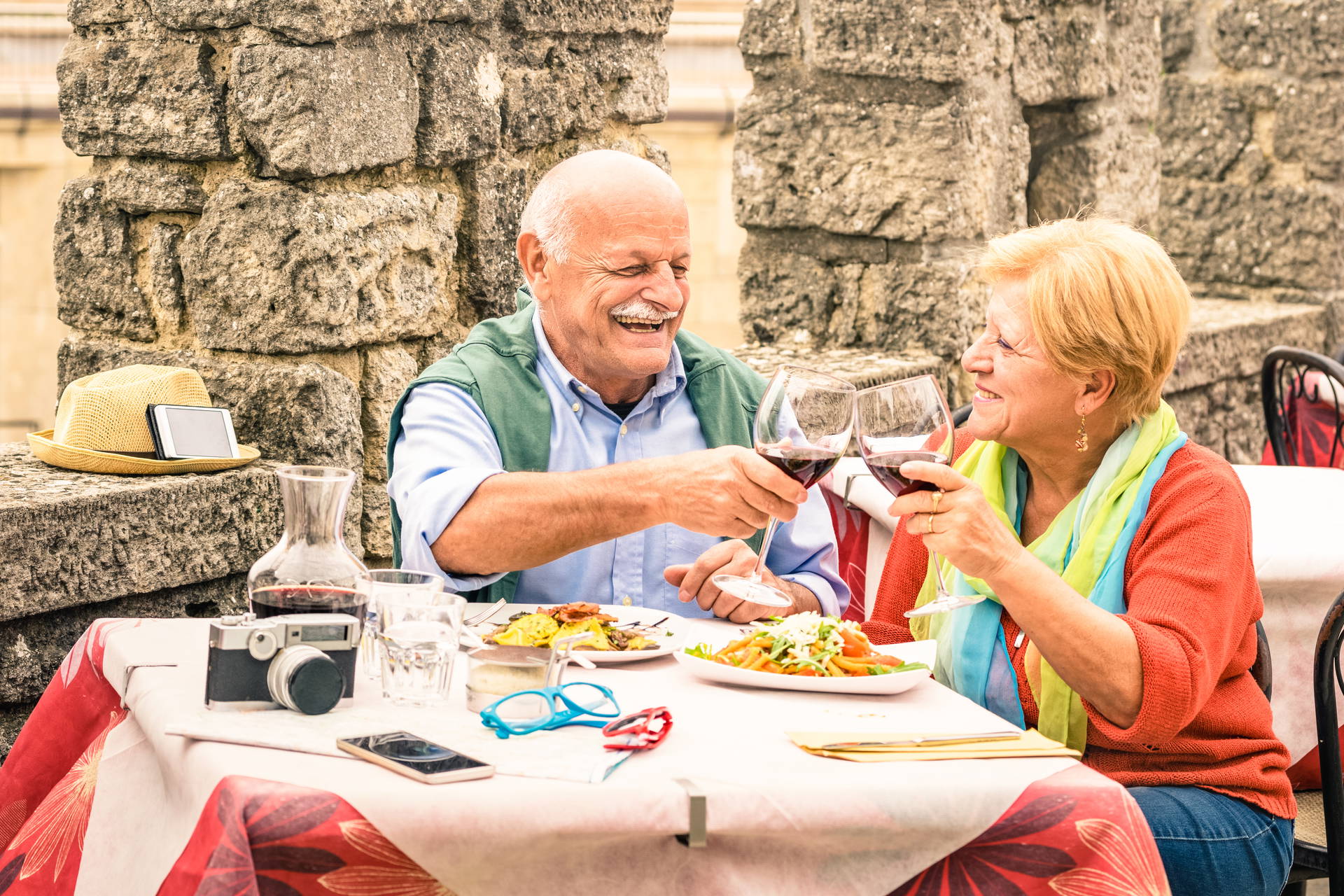 Uśmiechnięta para seniorów w restauracji wznosi toast czerwonym winem.