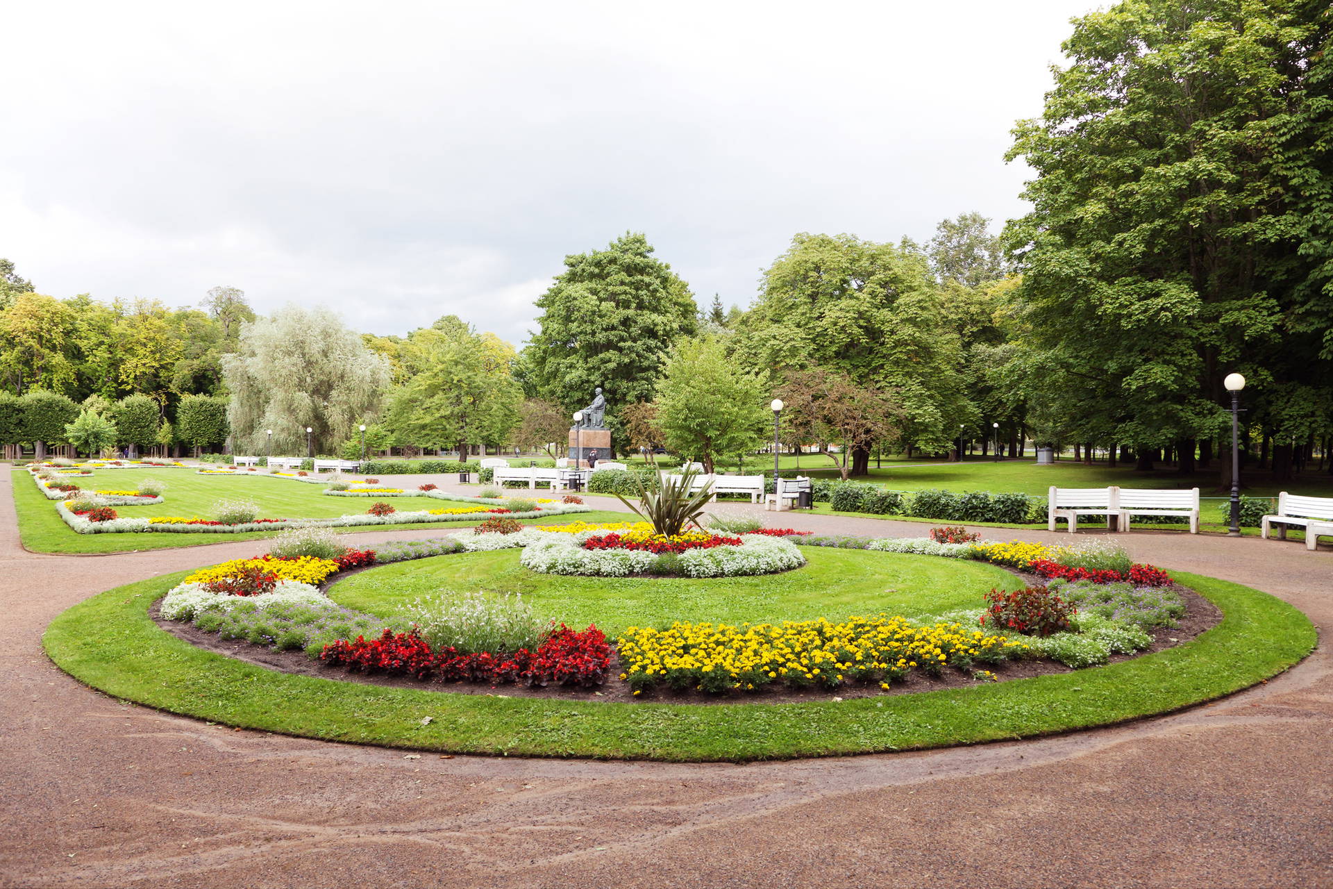 Park z klombami kwiatów, ławkami i pomnikiem.