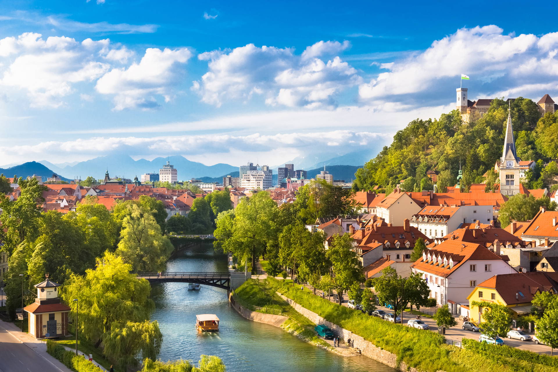 Panorama Lublany z rzeką, mostami i zamkiem na wzgórzu w tle.