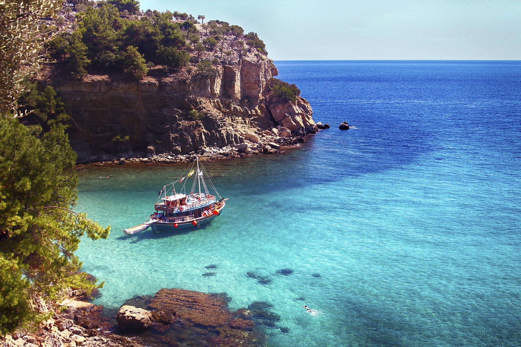 Łódź na turkusowej wodzie w zatoce, w tle klif.