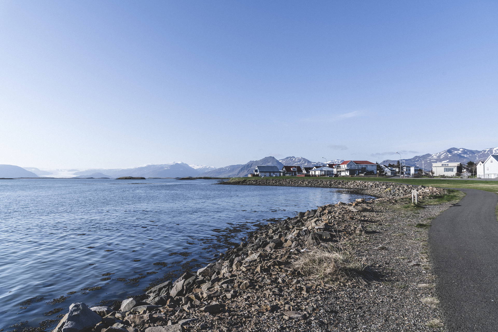 Islandzki krajobraz z domami nad morzem i górami w tle.