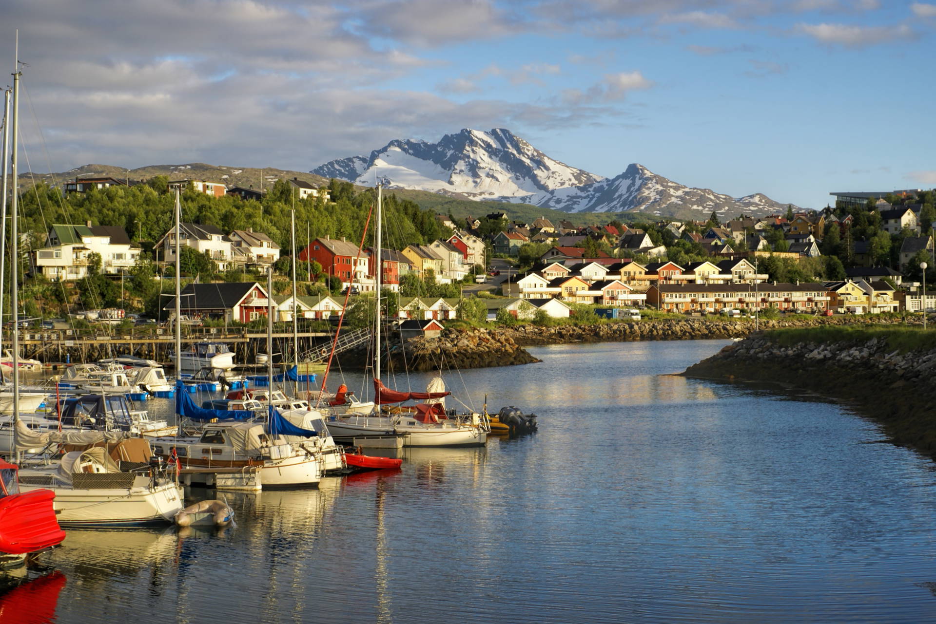 Port w Norwegii z łodziami i budynkami. W tle ośnieżona góra.