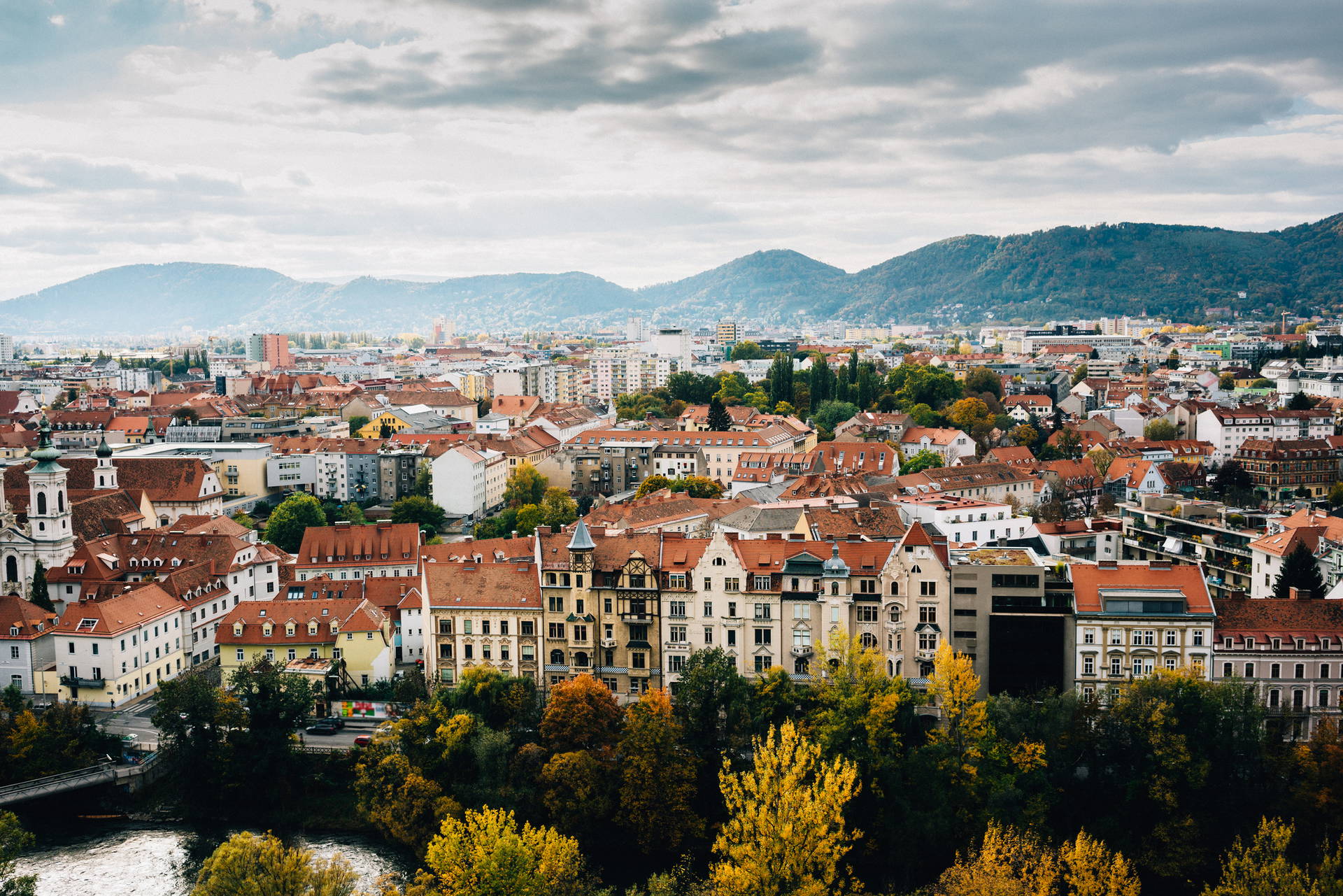 Panorama miasta Graz w Austrii z czerwonymi dachami budynków i górami w oddali.