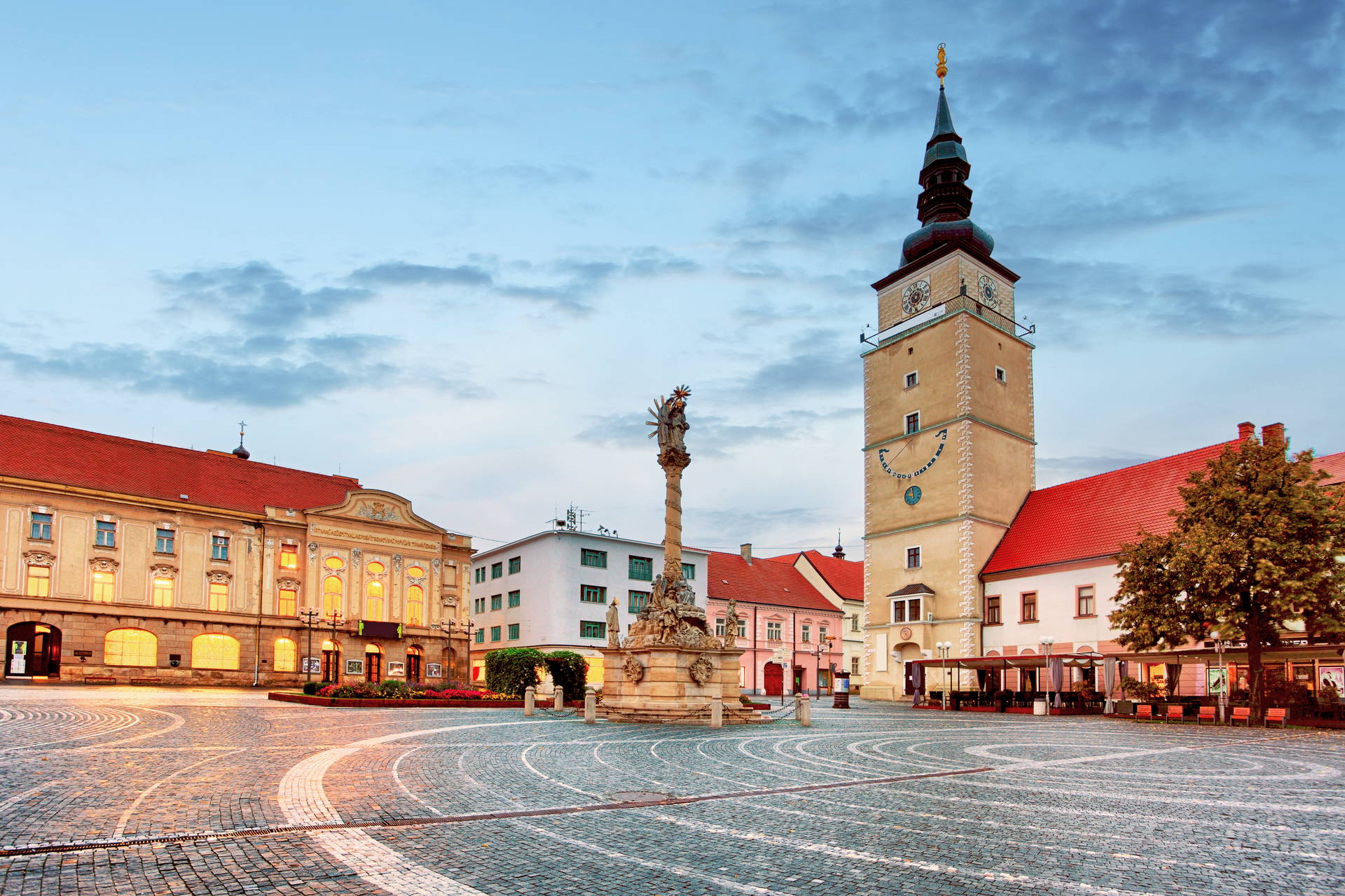 Rynek w Trnawie na Słowacji o zmierzchu. Widok na oświetloną Wieżę Miejską, Kolumnę Trójcy Świętej i kamienice.