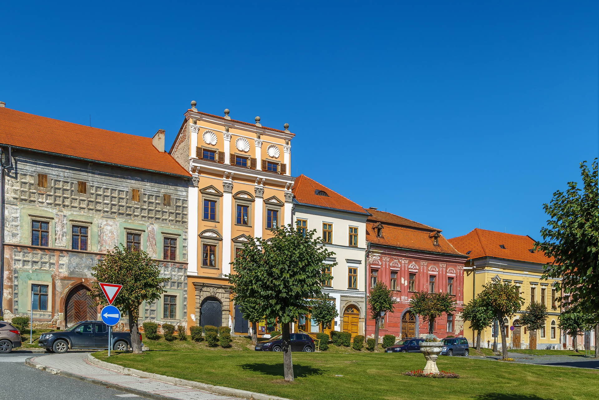 Rząd kolorowych kamienic na tle zielonego skweru w Telczu.