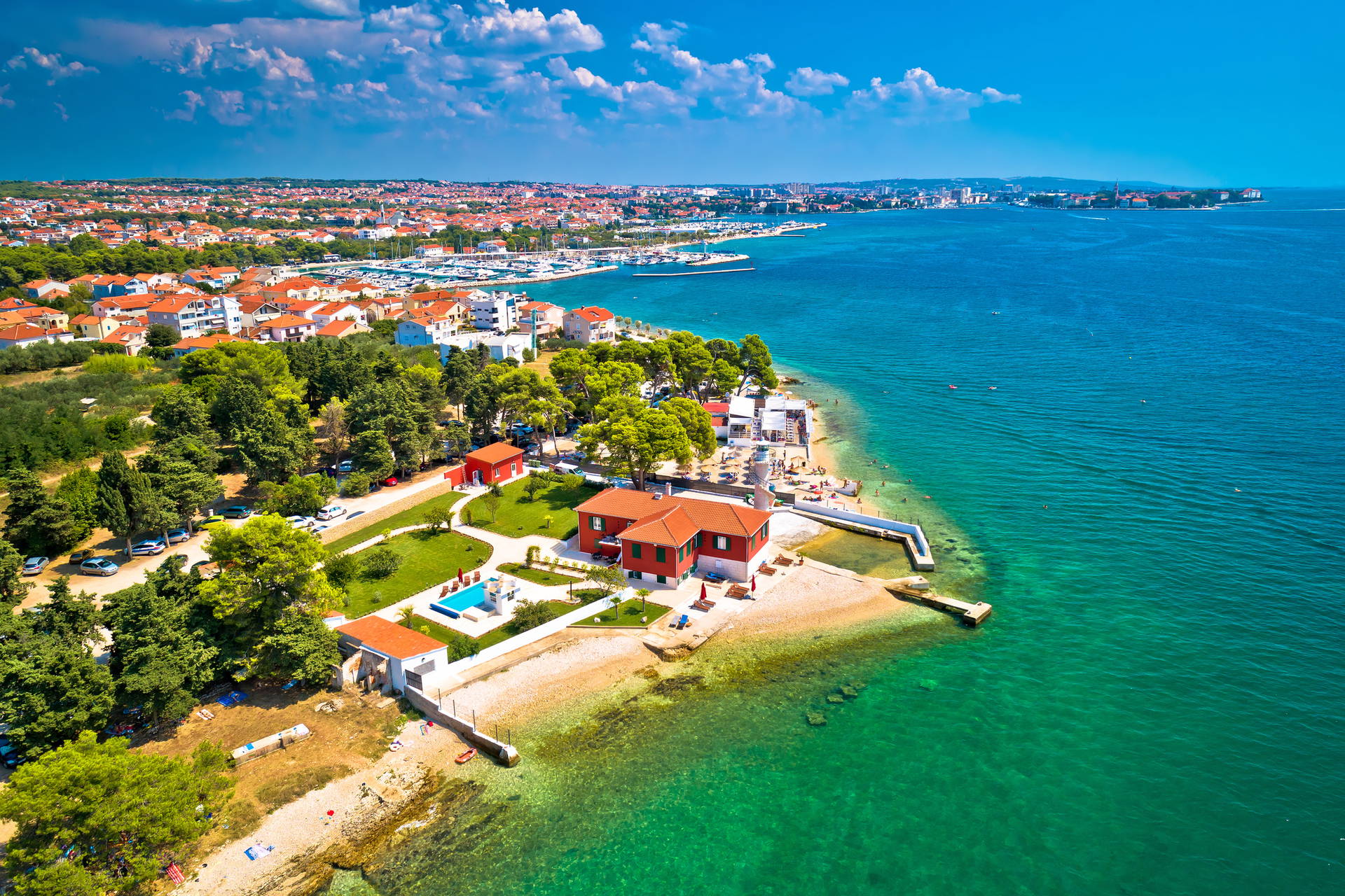 Widok z lotu ptaka na Zadar w Chorwacji. Turkusowa woda oblewa budynki z czerwonymi dachami.