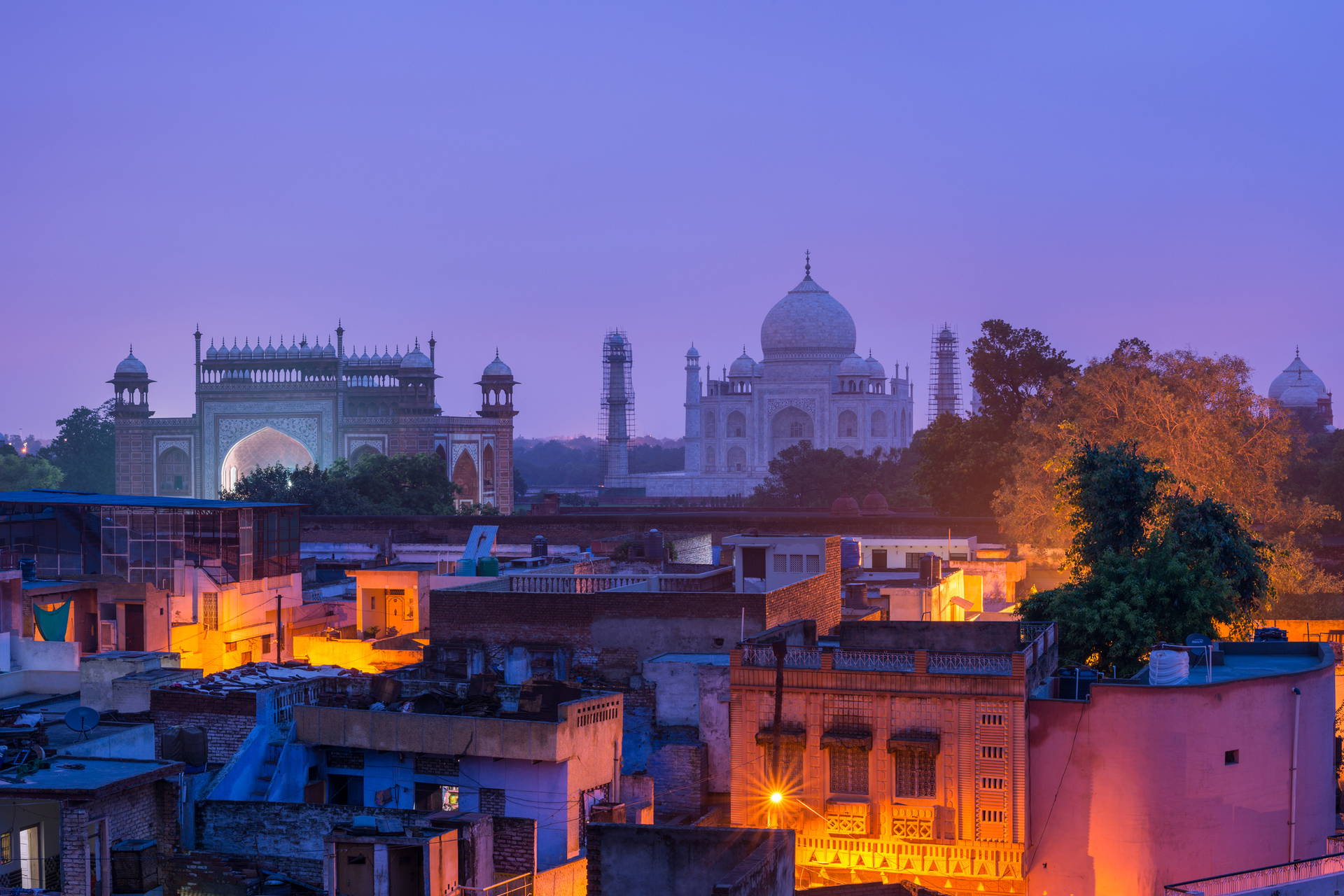 Nocny widok na Taj Mahal z zabudową miejską w tle.