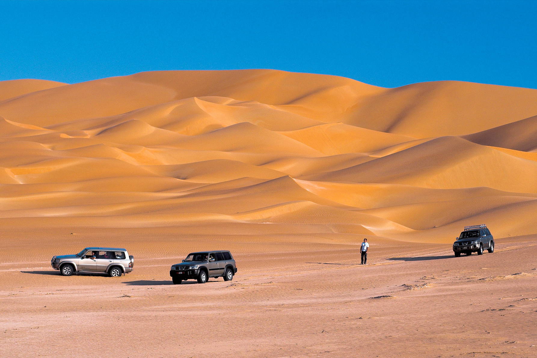 Trzy samochody na pustynnych wydmach.